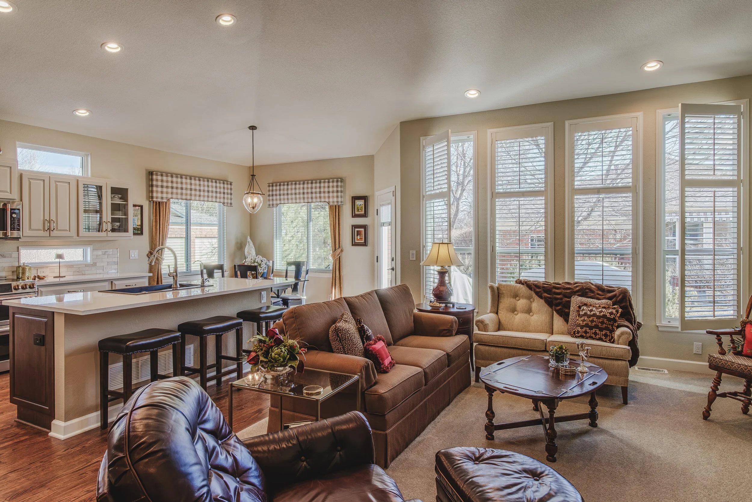 Open Concept living room with large windows, brown and cream furniture, and a eat-in kitchen in the background, shot in Longmont, Colorado by Context Images. 