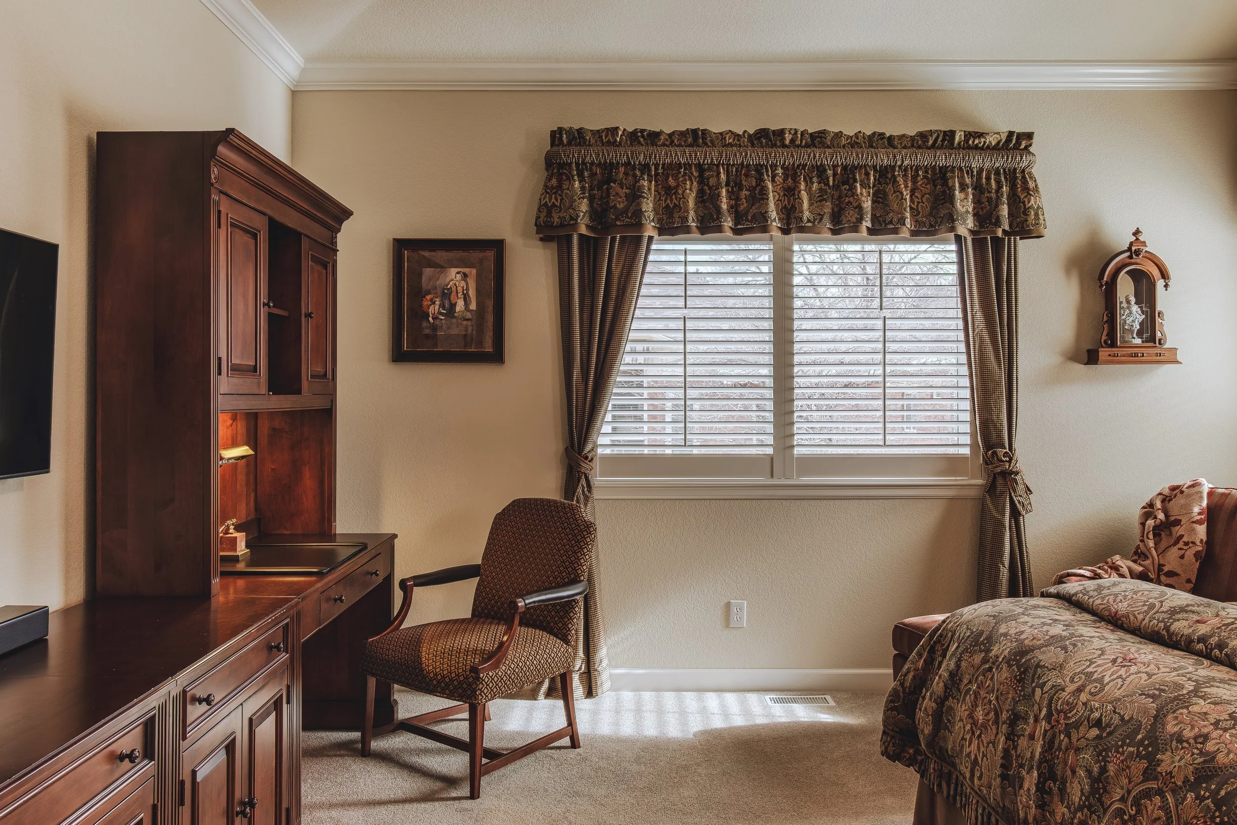 Sophisticated bedroom office with a window dressed in patterned curtains, a wooden desk set, and an upholstered armchair, shot in Longmont, Colorado by Context Images.
