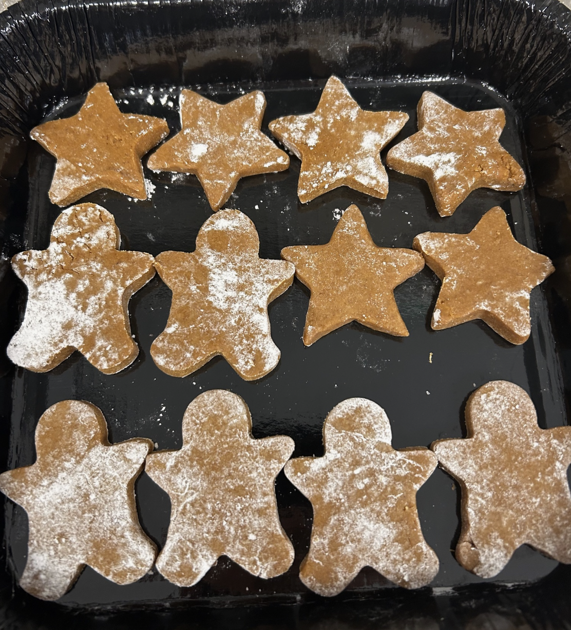 Star-shaped and teddy bear-shaped cookies dusted with powdered sugar in a baking tray.