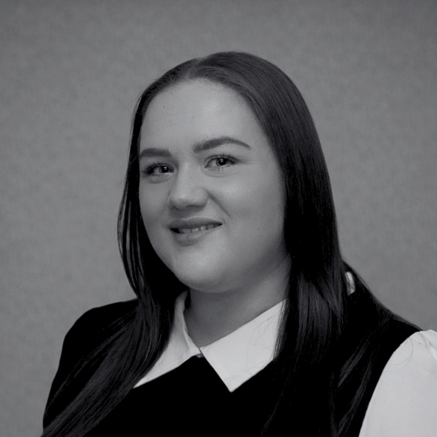 Black and white portrait of a woman with long, straight hair wearing a collared shirt and a sleeveless top, smiling slightly against a plain background.