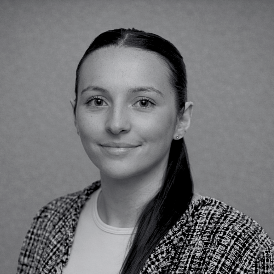 Black and white portrait of a smiling woman with dark hair tied back, wearing a patterned blazer and a light top, against a plain background.