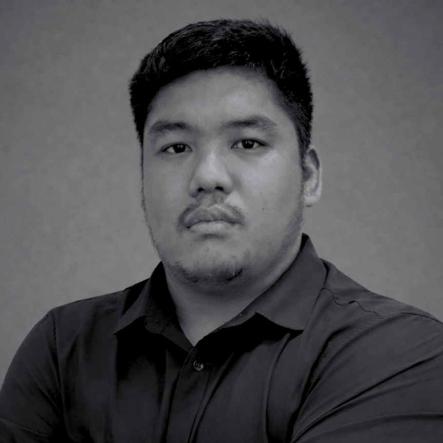 Black and white portrait of a young man with short dark hair, wearing a button-up shirt, looking directly at the camera against a plain background.