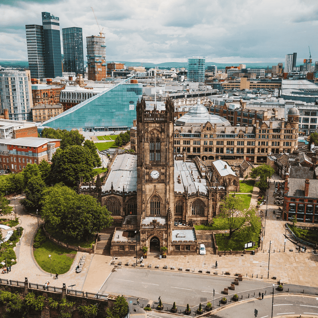 Aerial view of a historic church with a clock tower in a city with modern high-rise buildings in the background.