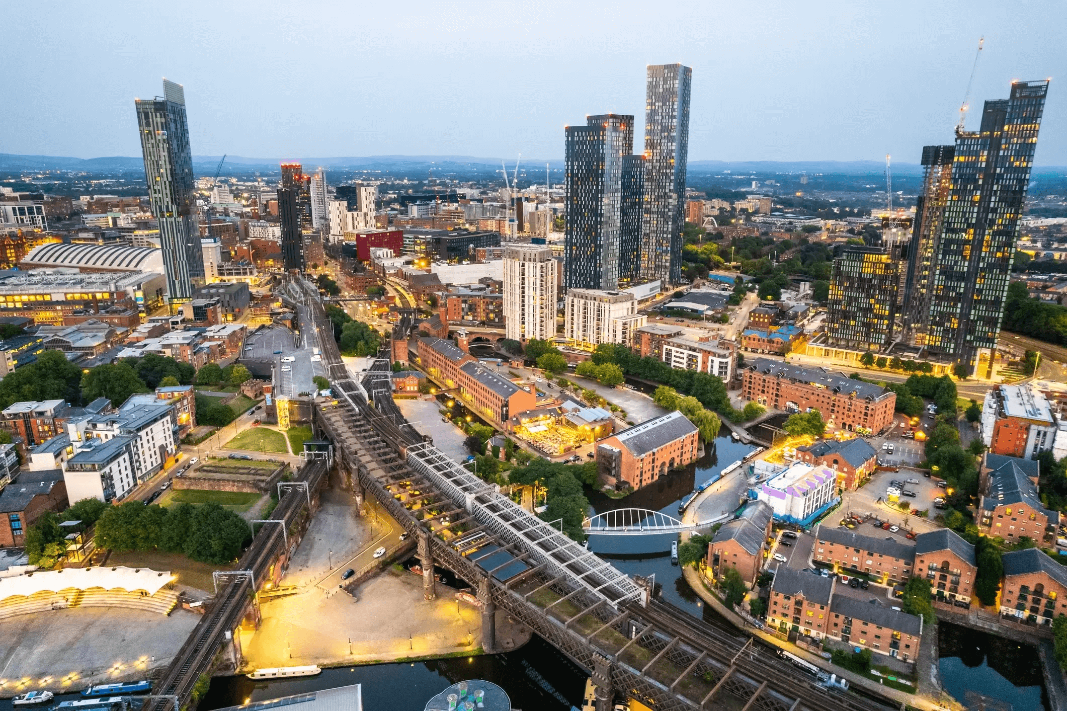 Aerial view of downtown Nashville, Tennessee at dusk featuring skyscrapers, bridges over a river, and city streets illuminated by lights.