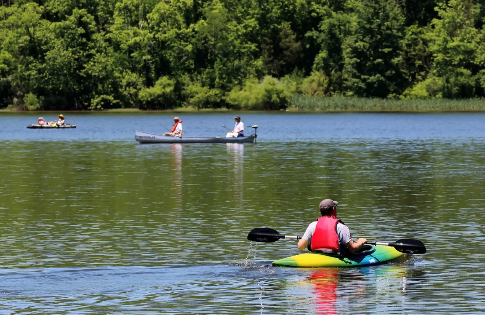 People kayaking and paddleboarding on a lake with green trees in the background on a sunny day.