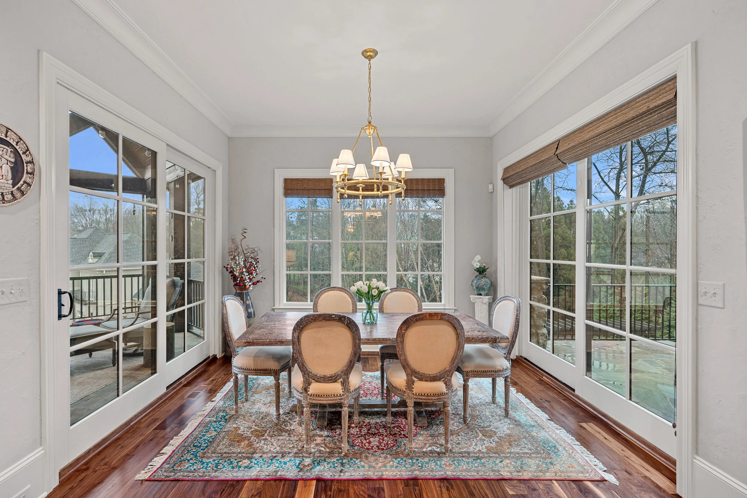 Dining room with a wooden table, six upholstered chairs, large windows, and a chandelier.