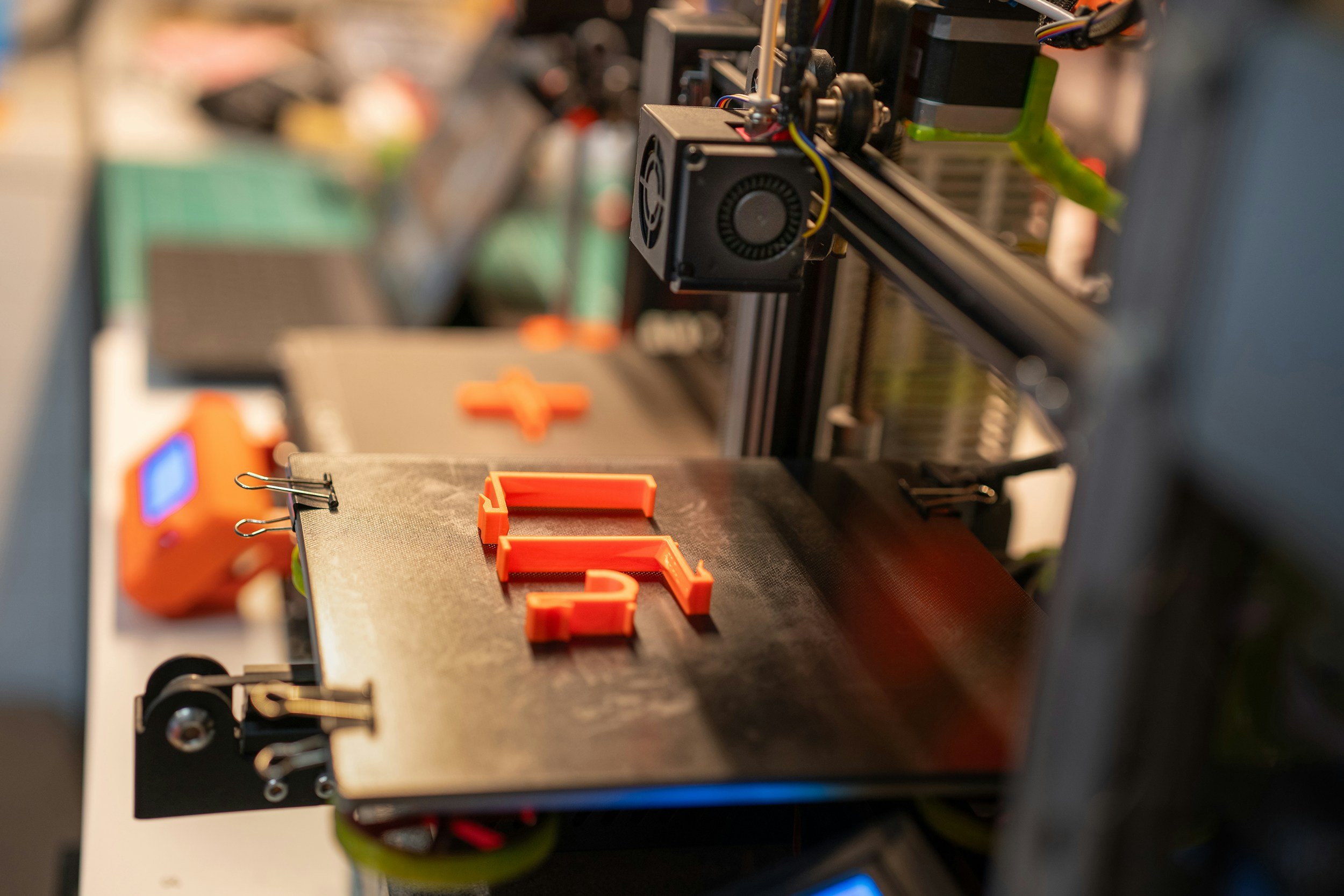 A 3D printer creating orange plastic objects on its build platform.