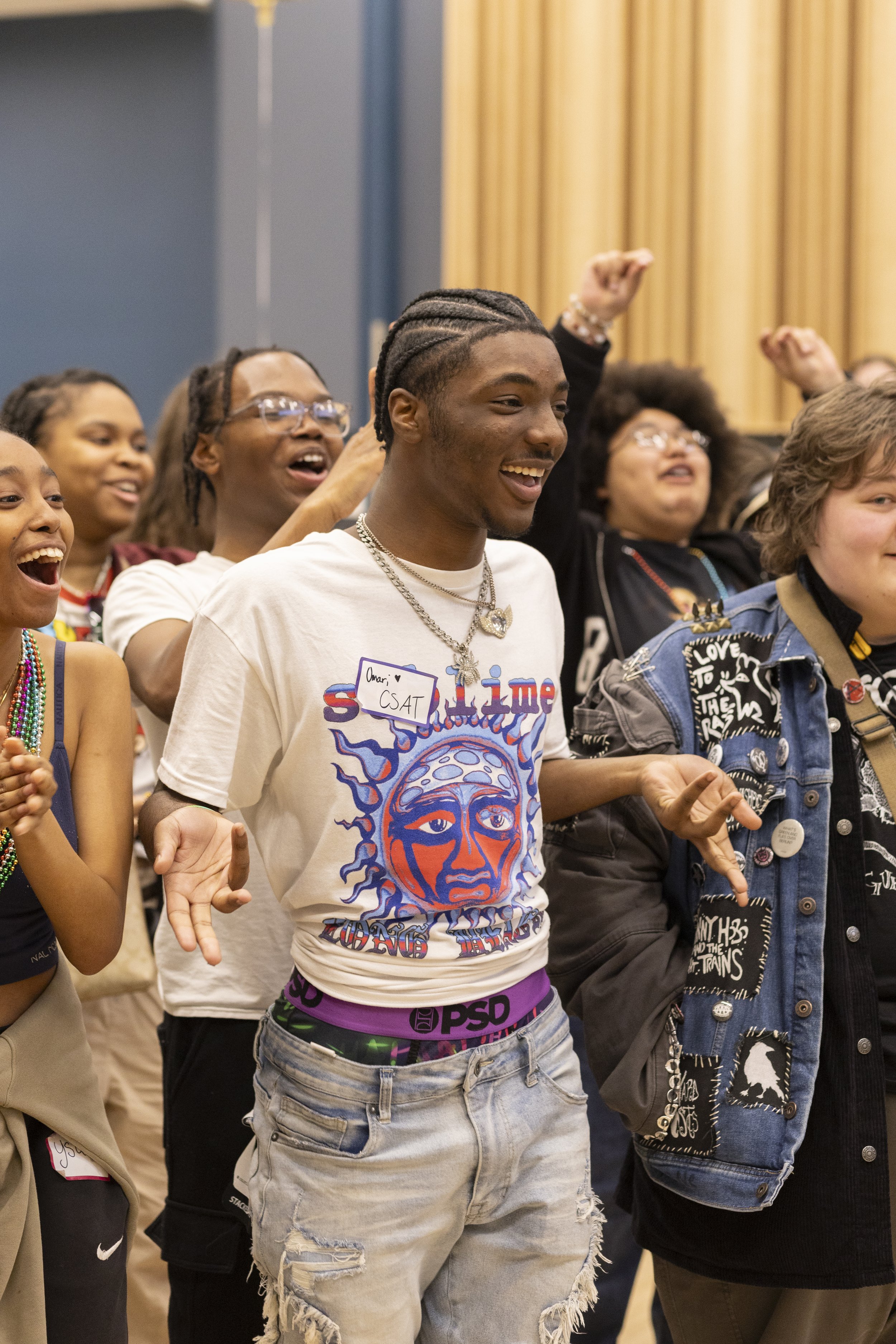 Group of diverse young people at an event, smiling and raising their hands with excitement.