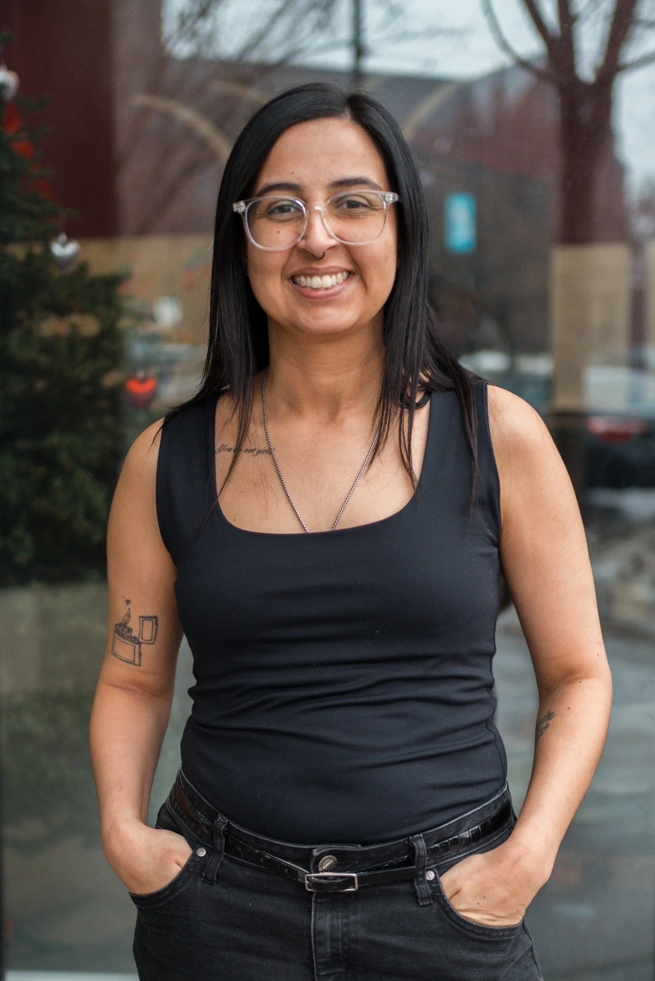 A woman with long dark hair smiling, wearing a black shirt, standing inside a house near a doorway.