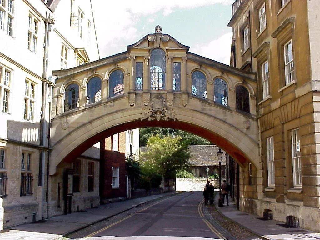 Stone bridge archway with ornate detailing and windows connecting two historic buildings in a narrow street.