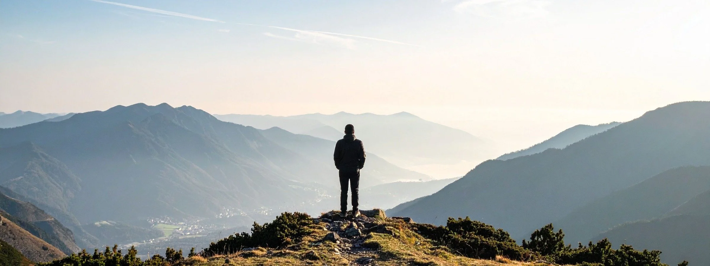 man stands on mountain top considering the view