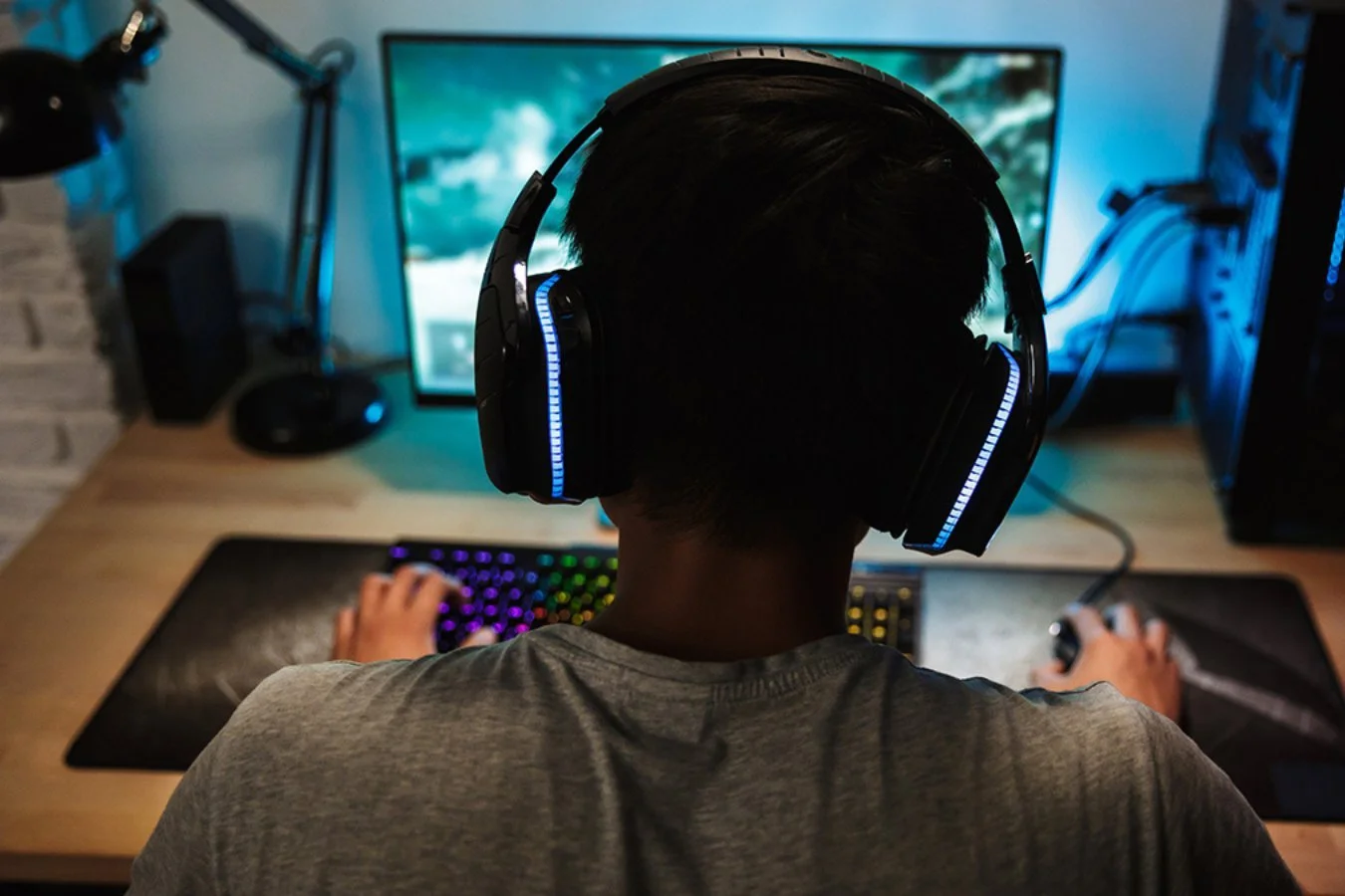 Back of a teenage boy wearing headphones while gaming in a dark room with coloured lights