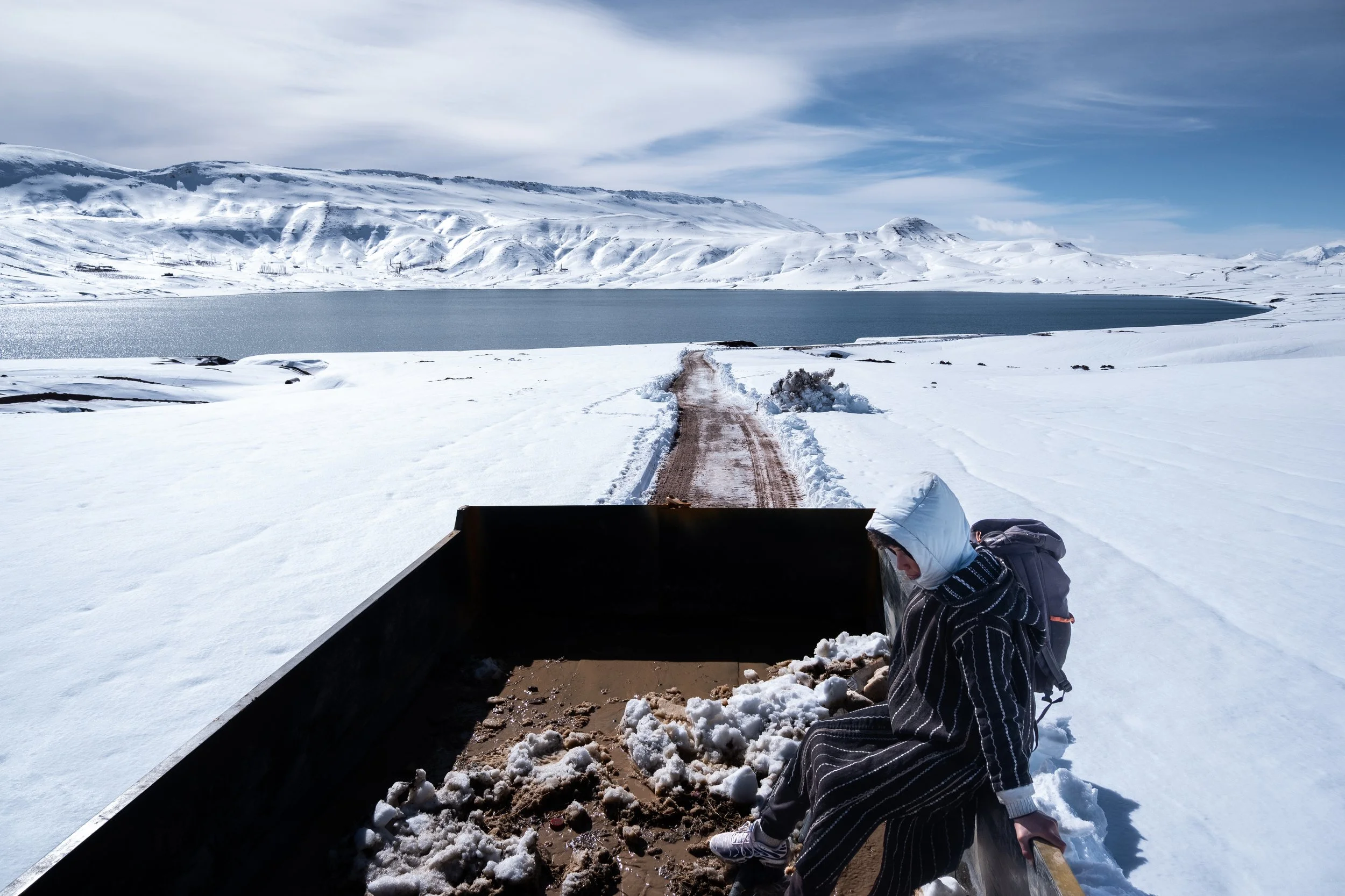 Near Imilchil, Morocco. Kamal and Saida travel in the back of a transport truck along a snow-lined mountain road, passing near Lake Isli.