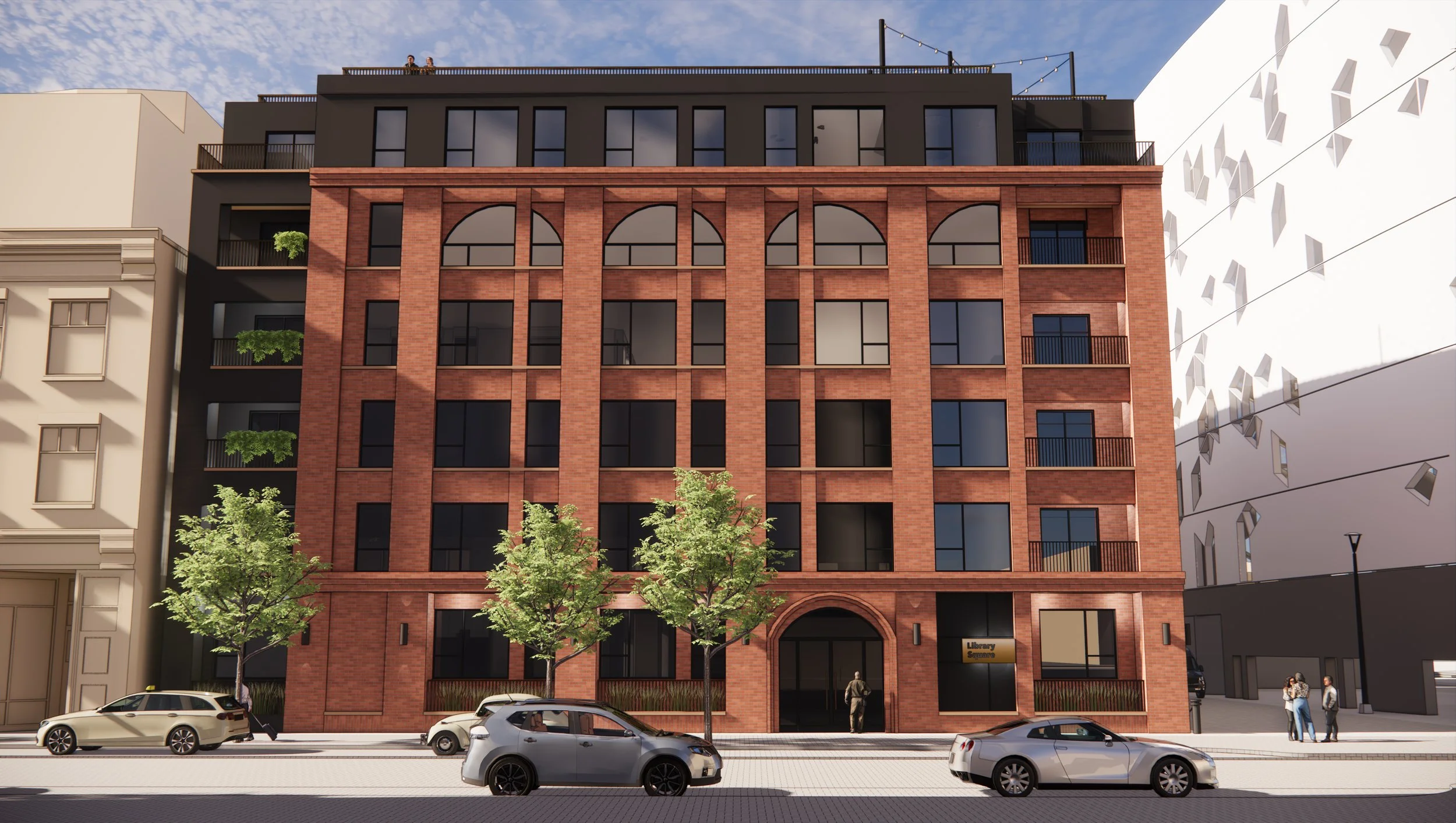 A modern urban building with a ground floor featuring an arched entrance and large windows, surrounded by trees and parked cars on the street.