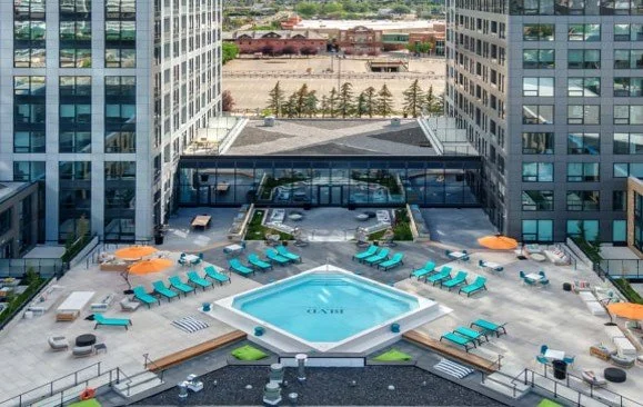 High-rise hotel courtyard with a central swimming pool surrounded by lounge chairs and umbrellas, cityscape in the background.