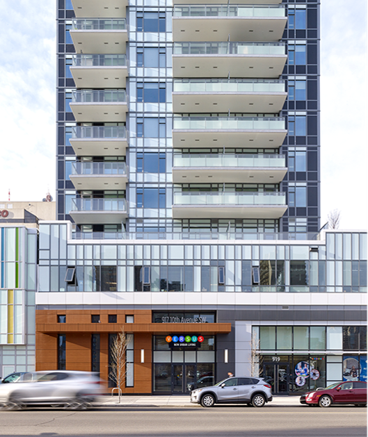 Modern multi-story building with glass balconies and commercial spaces on the ground floor on a city street.