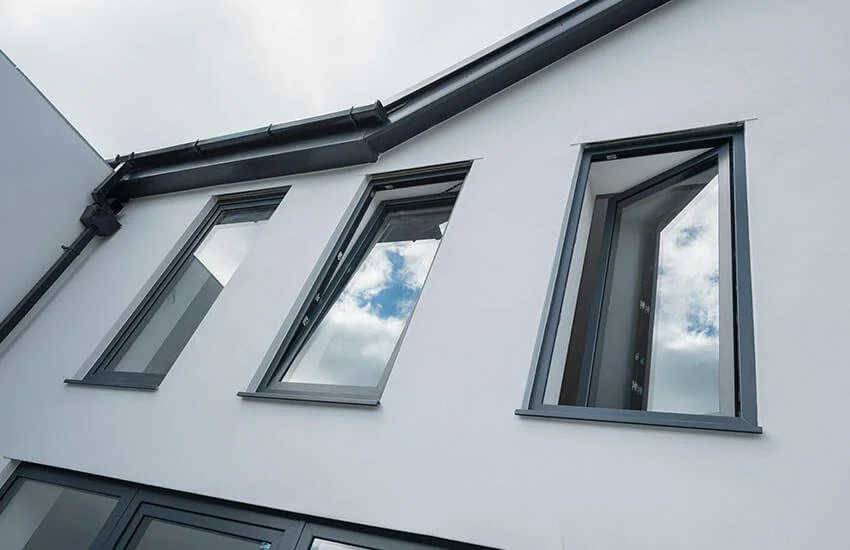 Modern white building with three open gray-framed windows and sky reflections.