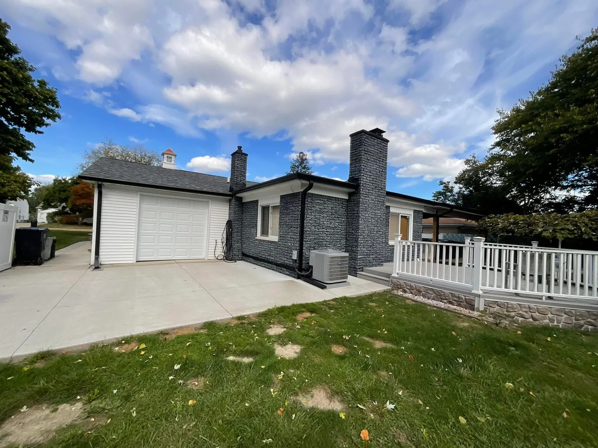 A house with a white garage door, chimney stacks, and a front porch with white railing. dads seamless gutters installed black gutters
