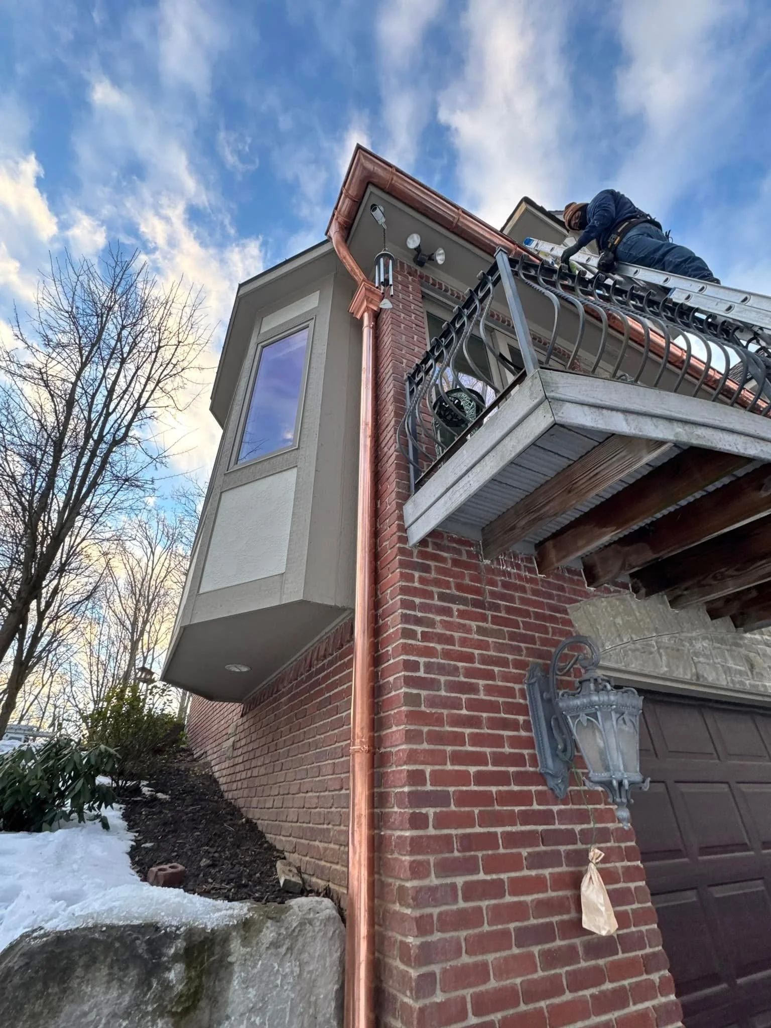 A dads seamless gutter installer on a ladder installing seamless copper gutters on the fascia of brick house with a copper downspout, a decorative  letter head stamped with dads seamless gutters