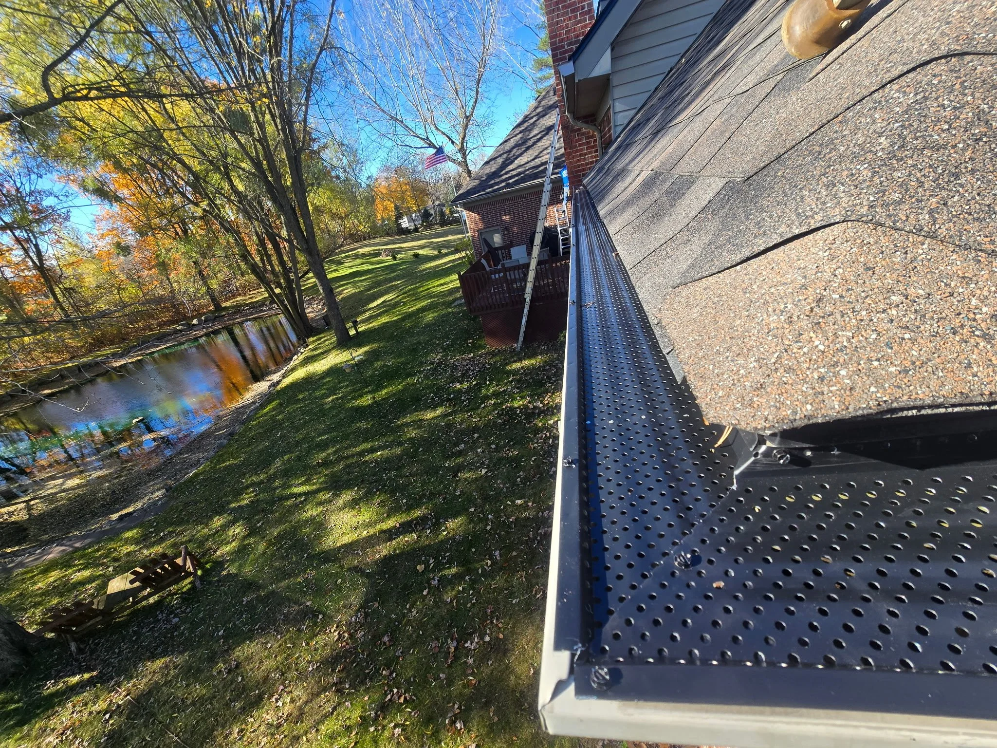 View of a house's roof showing a gutter guards installed by dad's seamless gutters along the edge, with a ladder leaned against the house, overlooking beautiful yards. dads seamless gutters installed,bloomfield hills Michigan