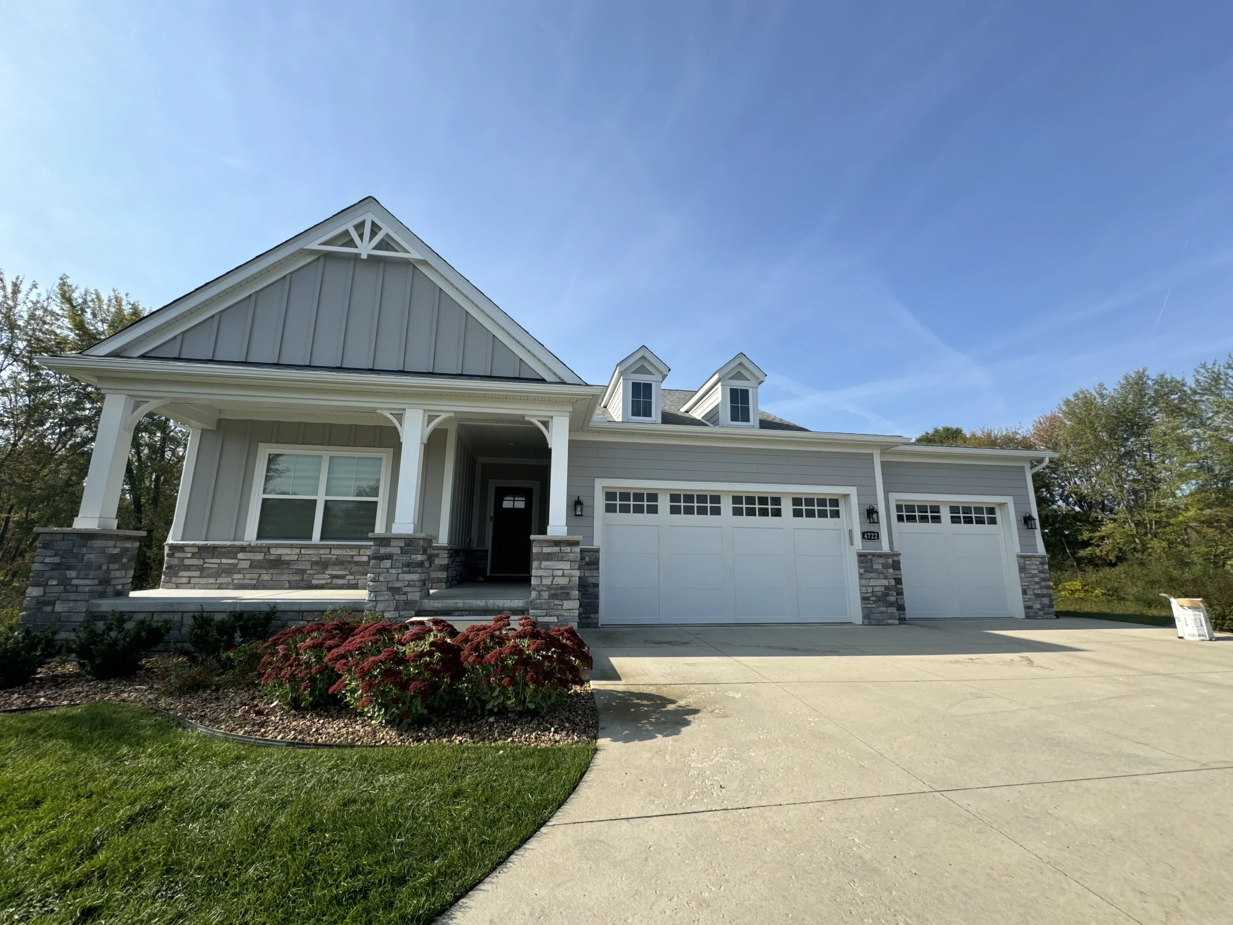 Front view of a modern suburban house with gray siding, stone accents, a driveway, newly built homes new sub-divisions hired dads seamless gutters for all seamless gutters