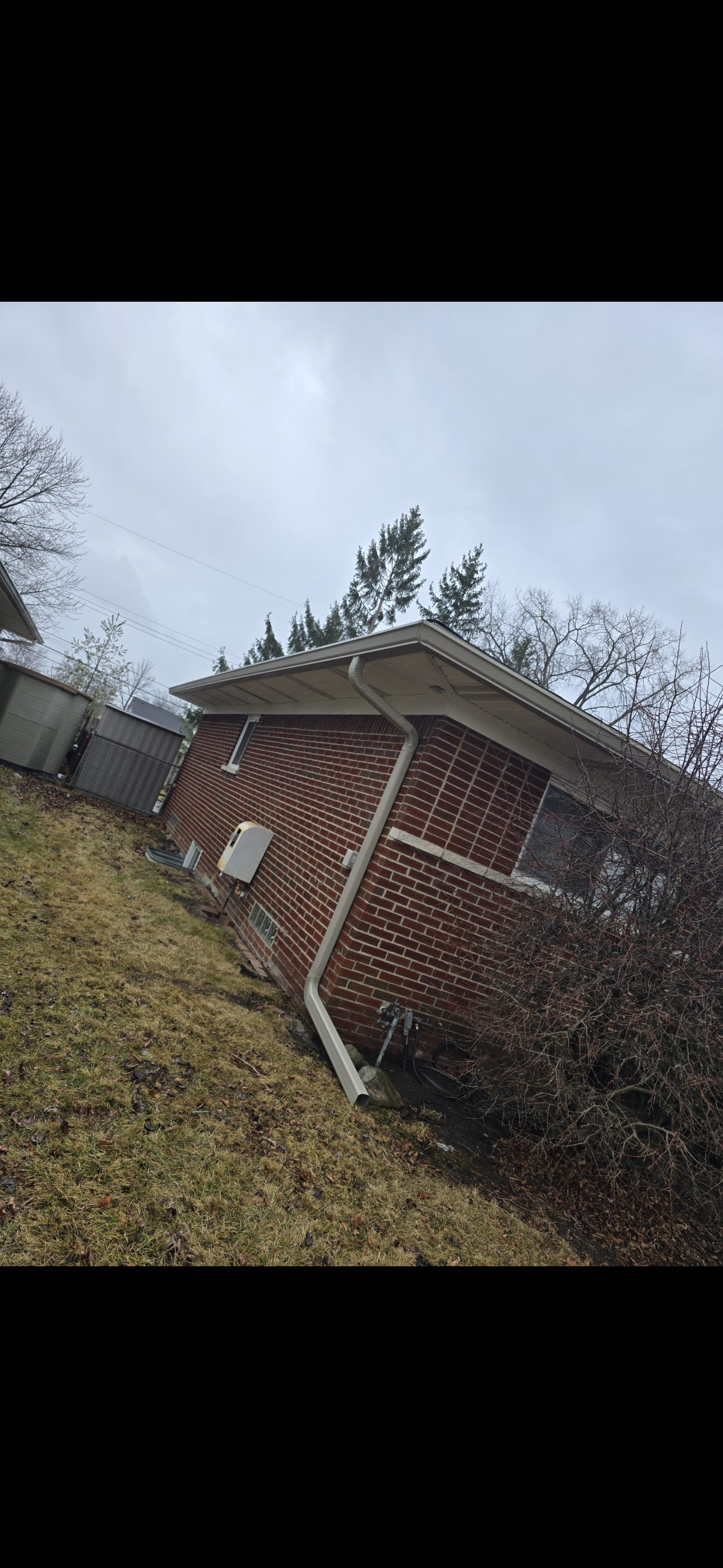 Side view of a brick house with a sloped roof, a new gutters with a downspout, installed by dads seamless gutters in the fall