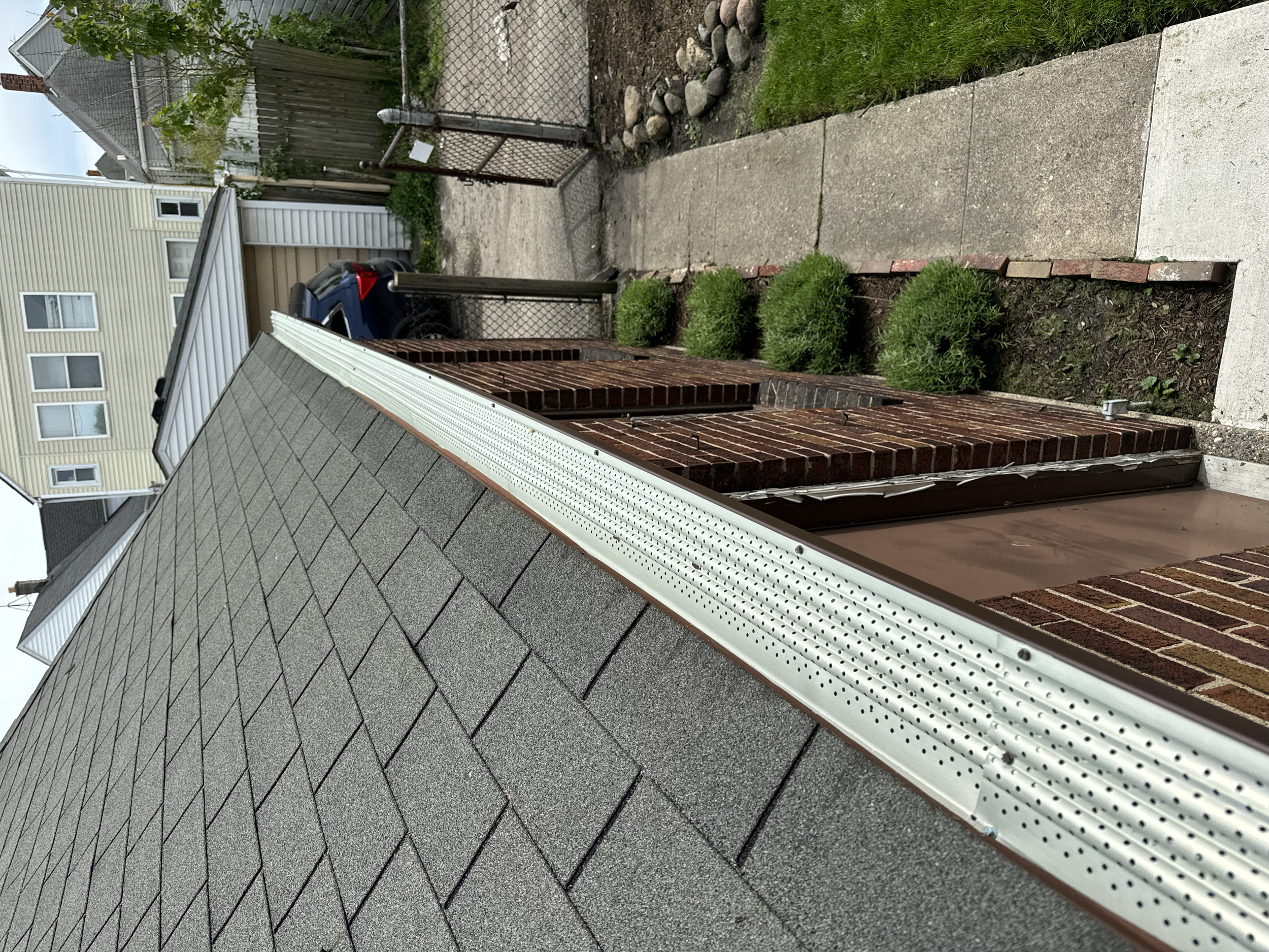Side view of a house with a gray shingle roof, brick walls, and a white gutters installed by dads seamless gutters and gutter guards installed by dads seamless gutters in Detroit michigan