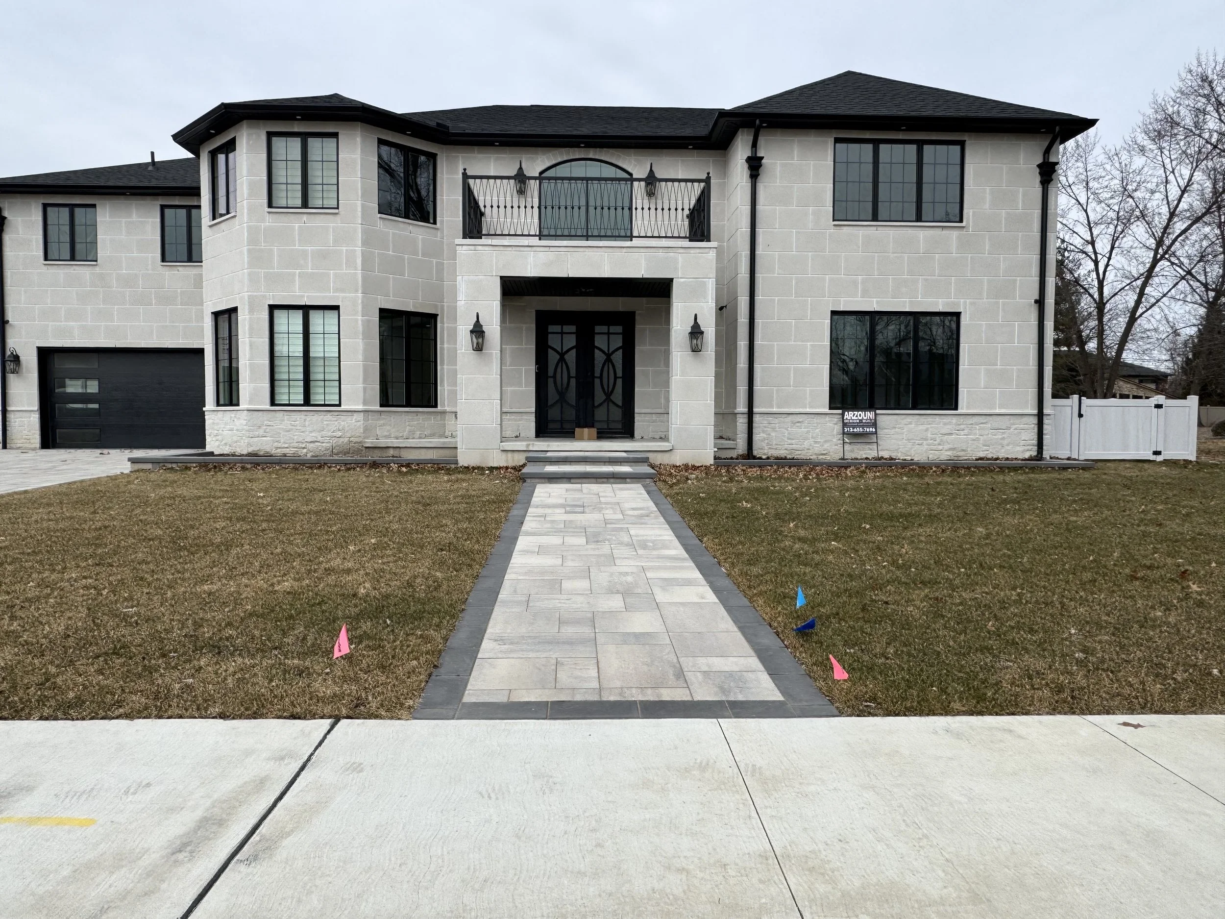 Front view of a modern two-story house with a paved walkway leading to the front door, a manicured lawn, and a small sign with contact informationFront view of a modern house with a concrete driveway, concrete pillars, and black commercial size gutte