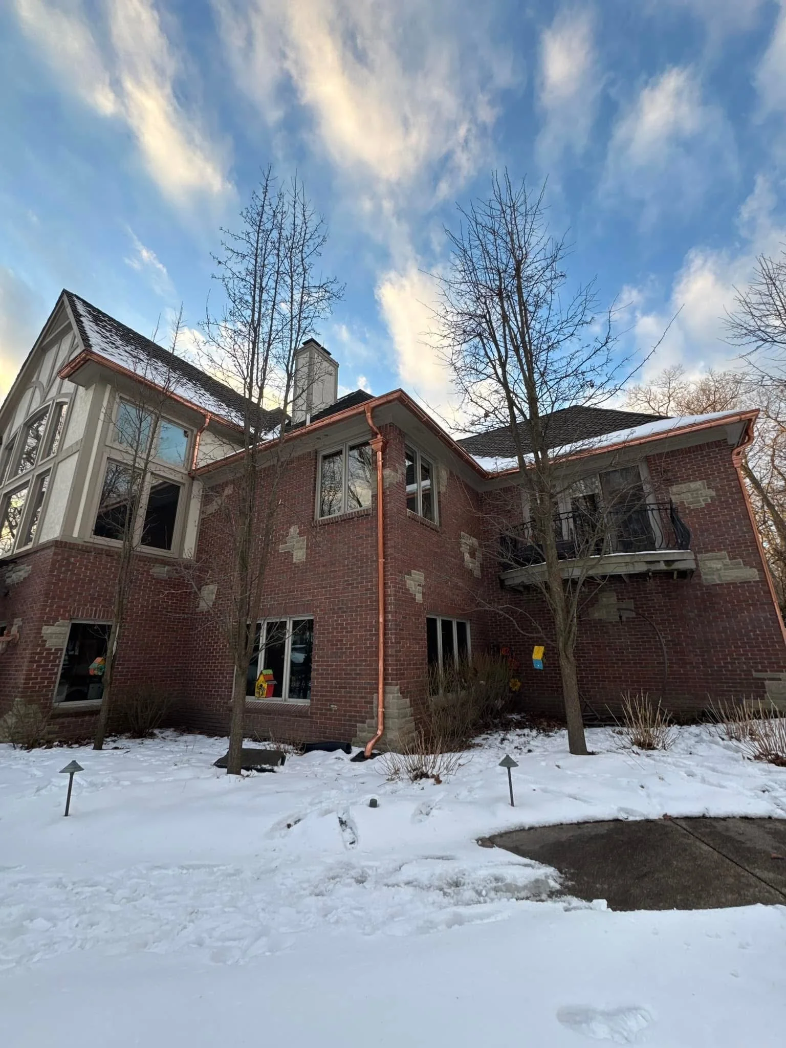 A large brick house with several windows and a balcony, set in a snowy yard in Milford michigan dads seamless gutters installed gutters on a multi-million dollar home, custom built and delivered hand installed by dads seamless gutters crew