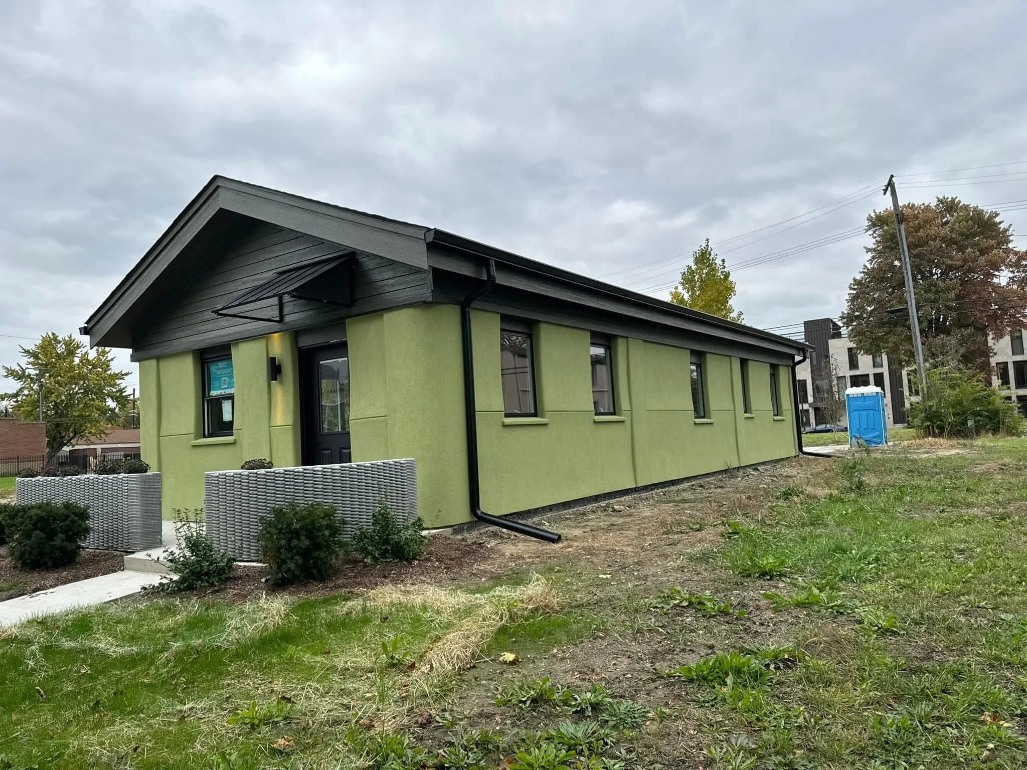 A small, modern house with a green facade and black roof, door, dad's seamless gutters worked with the city of detroit to complete its latest project 3D printed home. dads seamless gutters installed black k-style gutters