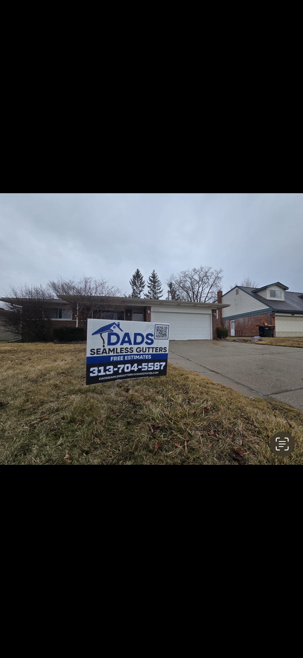 Front yard of a house with a sign advertising seamless gutter services from DADS, including contact information and website. 313-704-5587