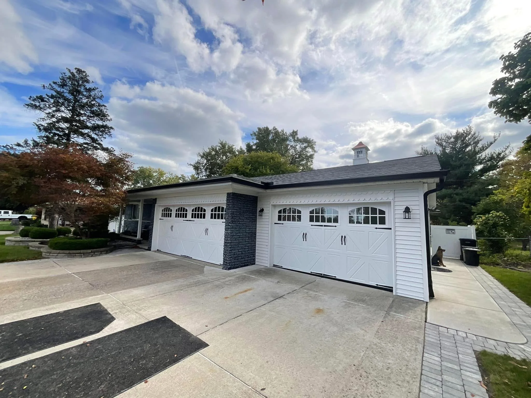 A white garage with two doors, a black brick column, and a sidewalk and driveway in front. dads seamless gutters worked on this newly built home installed black seamless gutters, white soffit and fascia .highly rated company for gutters,michigan