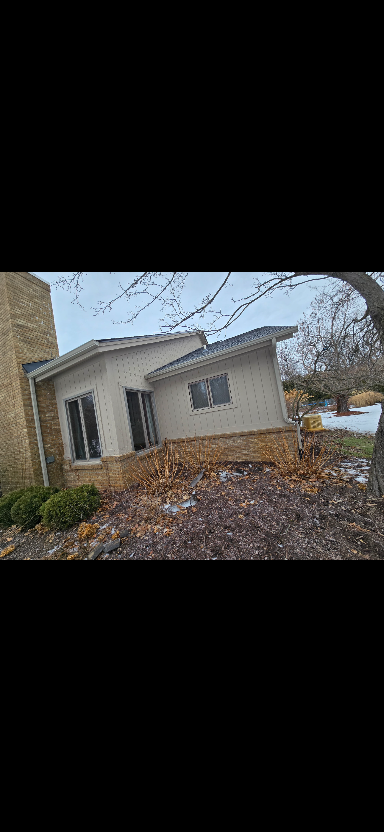 Exterior view of a residential house with a slanted roof, large windows, and brick foundation. dads seamless gutters installs year-round gutters in michigan