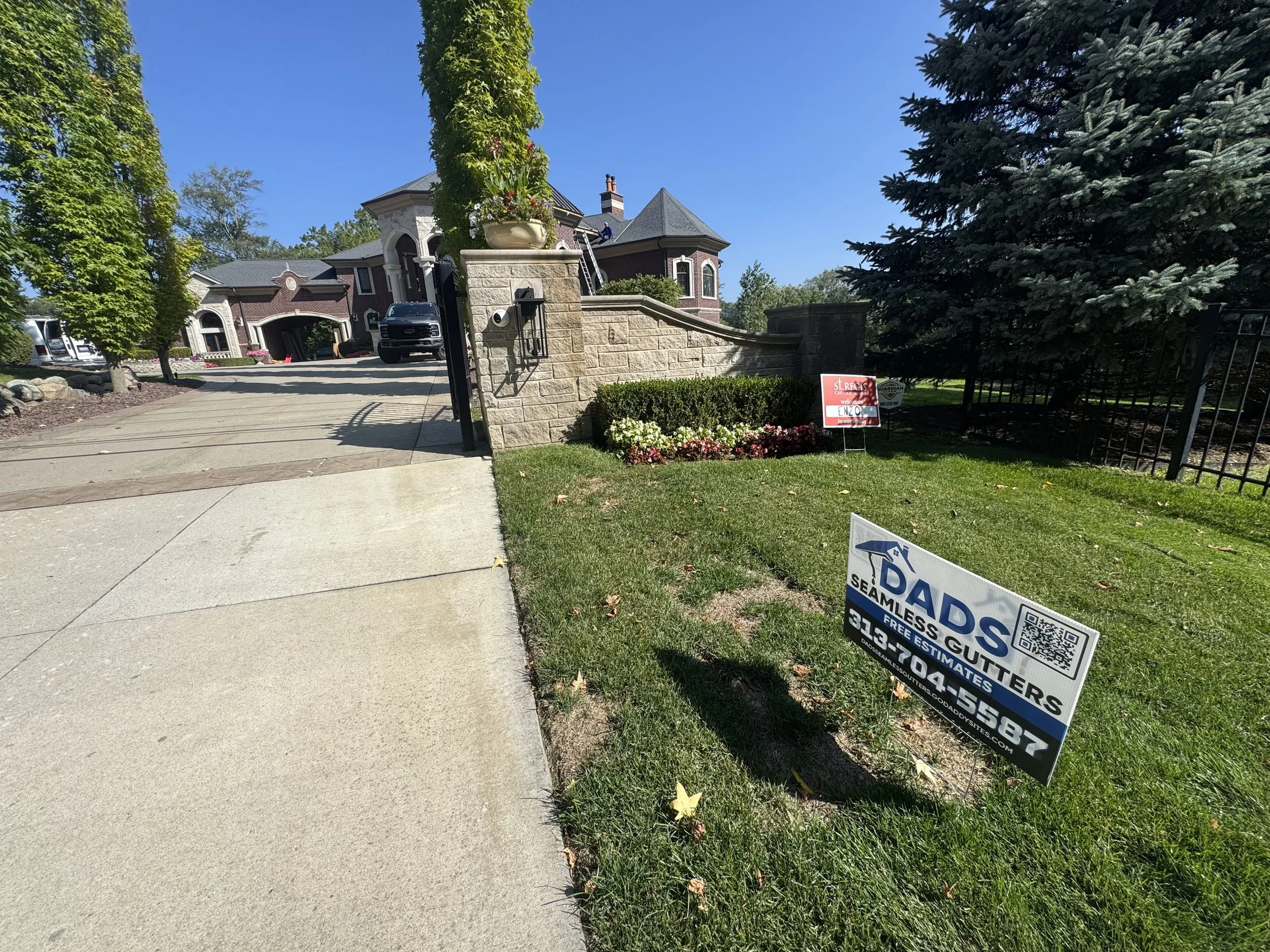 Residential sidewalk leading up to large house with landscaped yard, trees, and signs for gutter installation services in front yard. private million dollar home hired dads seamless gutters to do residential and commercial gutters.