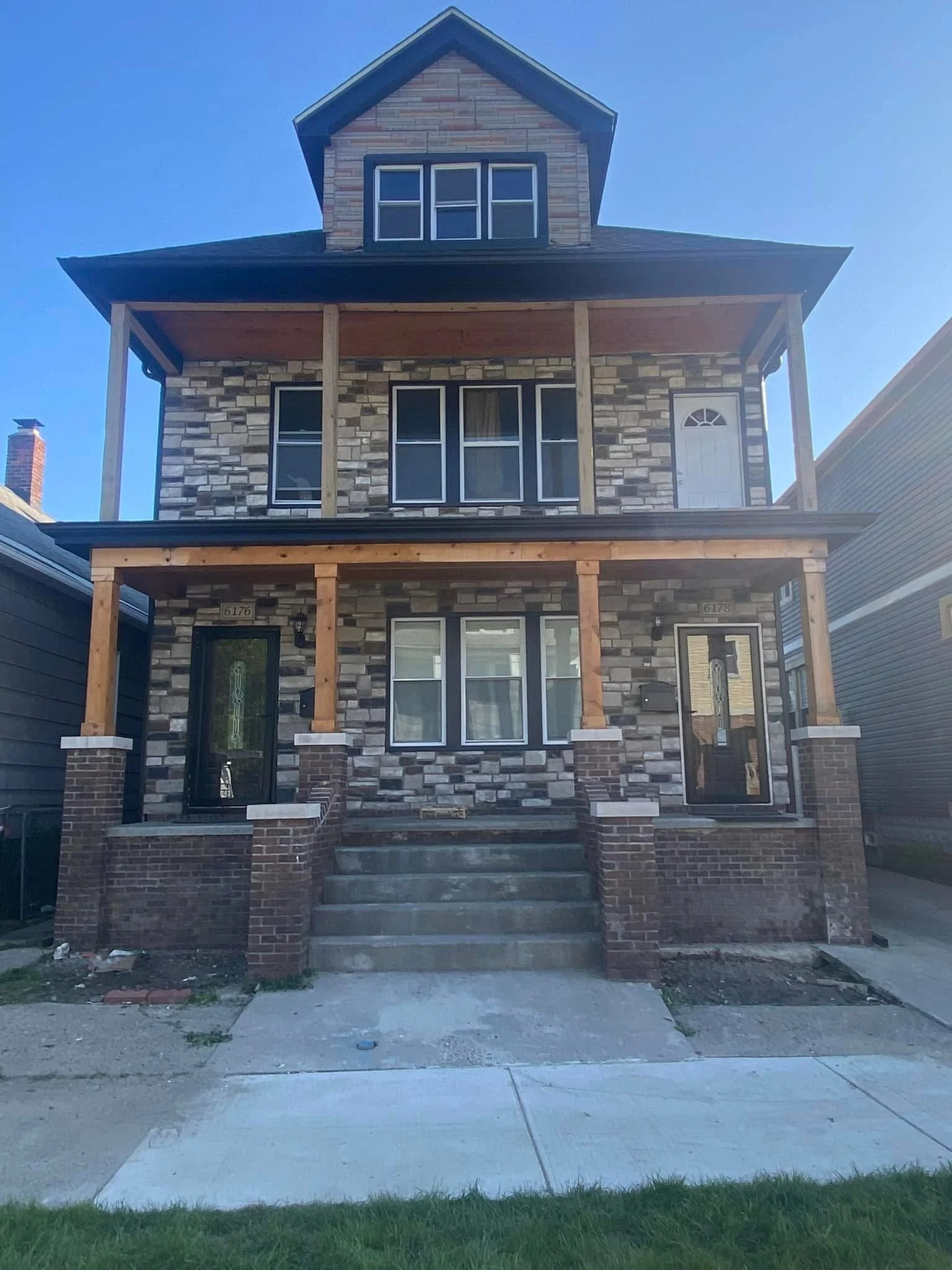 Front view of a three-story house under construction with brick and stone exterior, black framed windows, a front porch with wooden support beams, and seamless gutters installed by dads seamless gutters