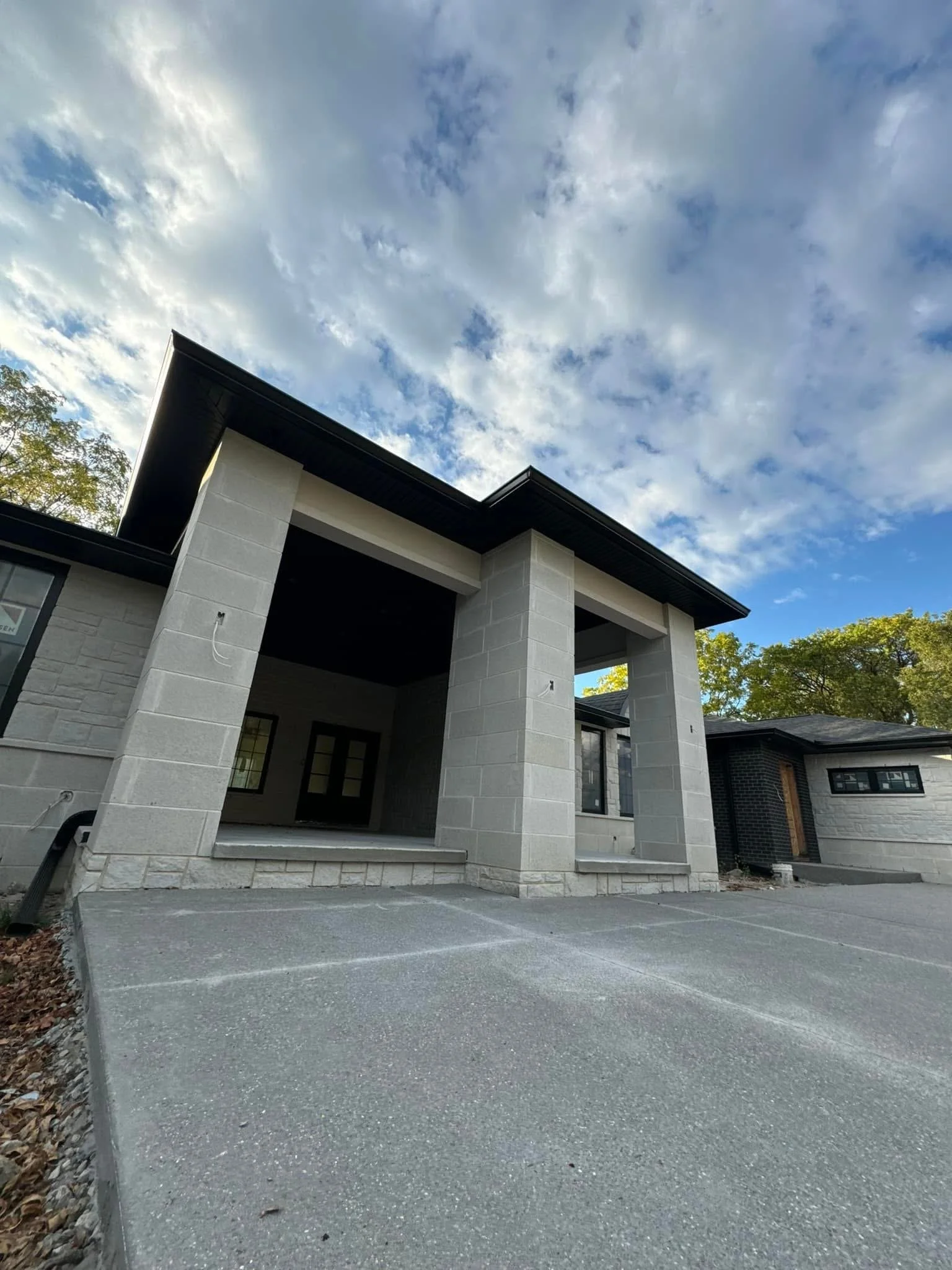 Front view of a modern house with a concrete driveway, concrete pillars, and black commercial size gutters installed by dads seamless guttes