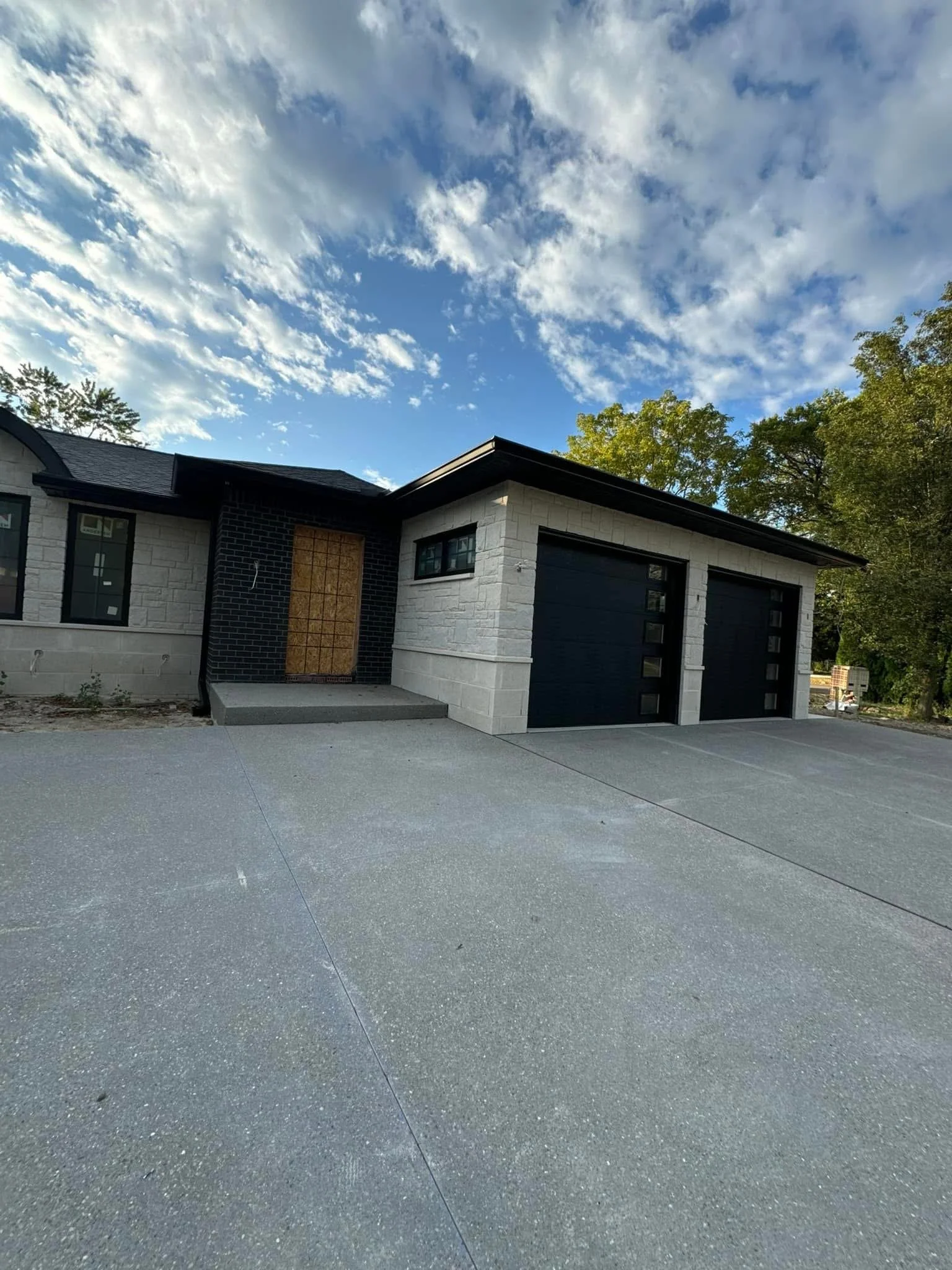 Front view of a modern house with a concrete driveway, concrete pillars, and black commercial size gutters installed by dads seamless guttes