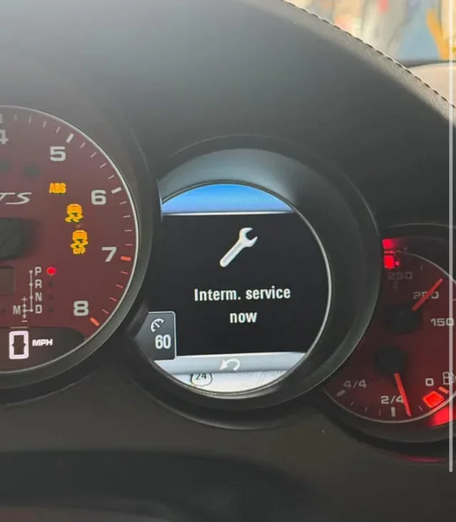 Car dashboard showing the message 'Interm. service now' on the central display, with warning lights on the left indicating vehicle issues, and gauges on the right displaying fuel level and engine temperature.