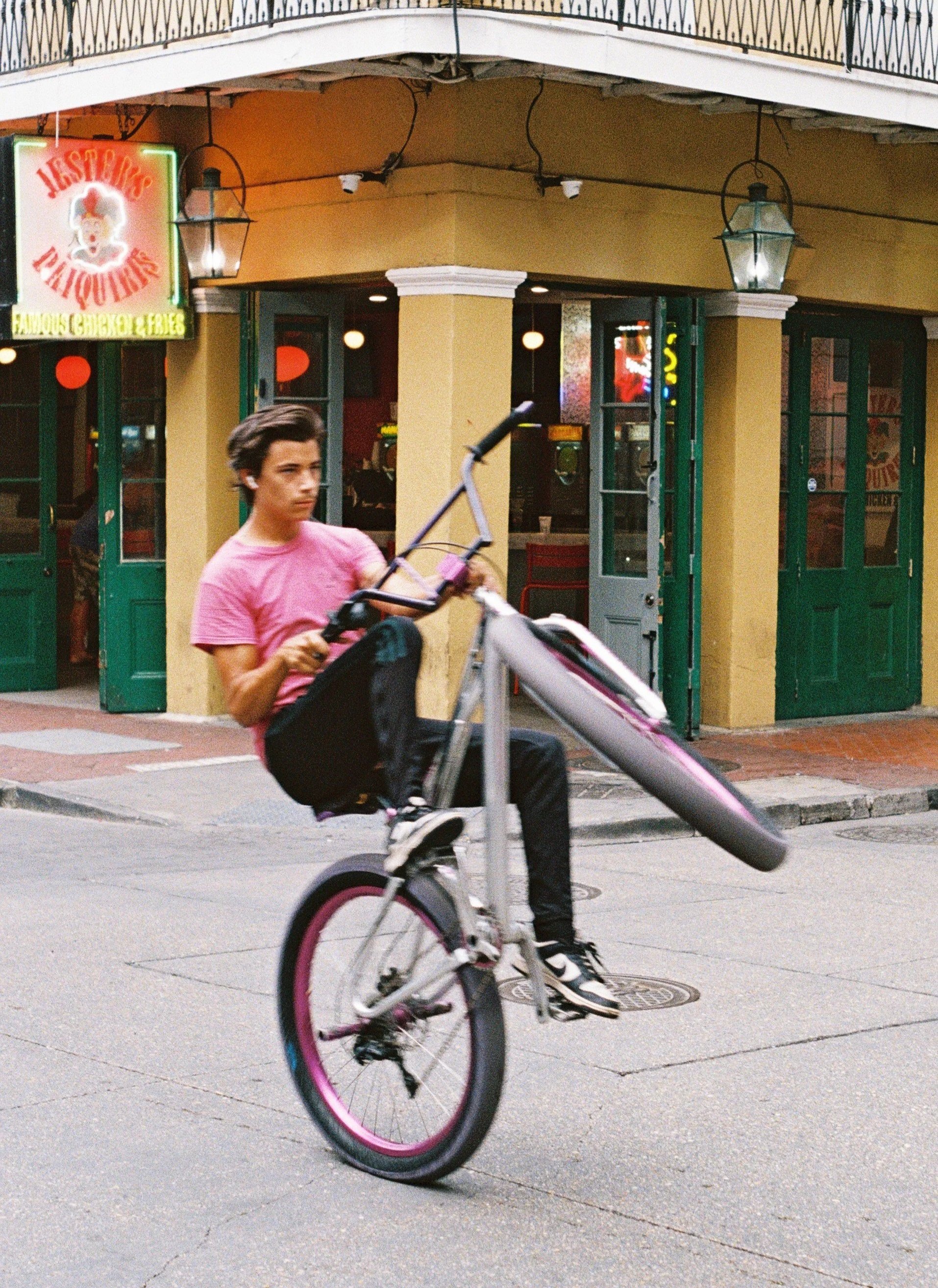 Young man performing a wheelie on a bicycle in front of a colorful restaurant with a yellow exterior and green doors.