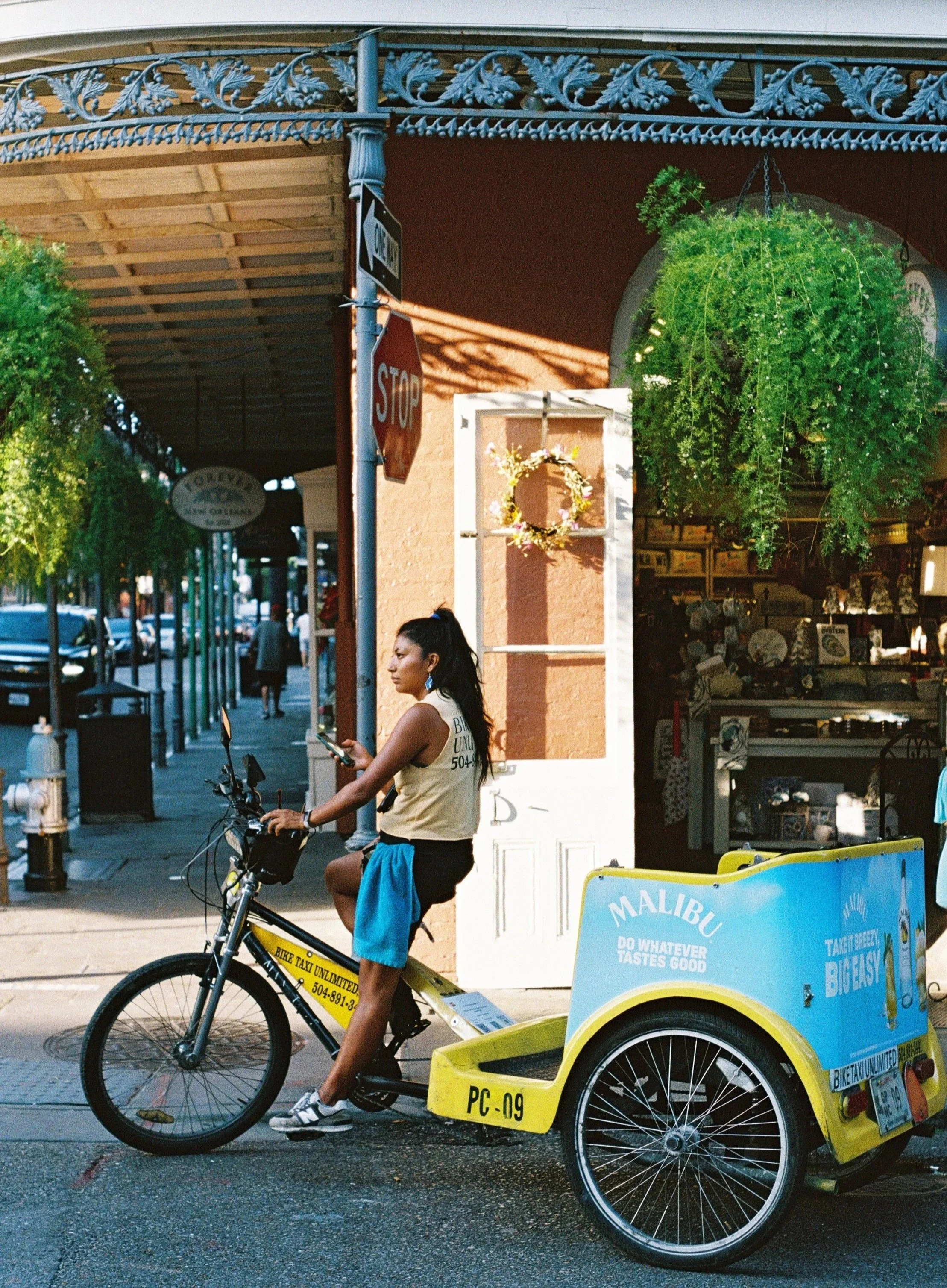 Woman sitting on a bike taxi in New Orleans, with a storefront and hanging green plants in the background.