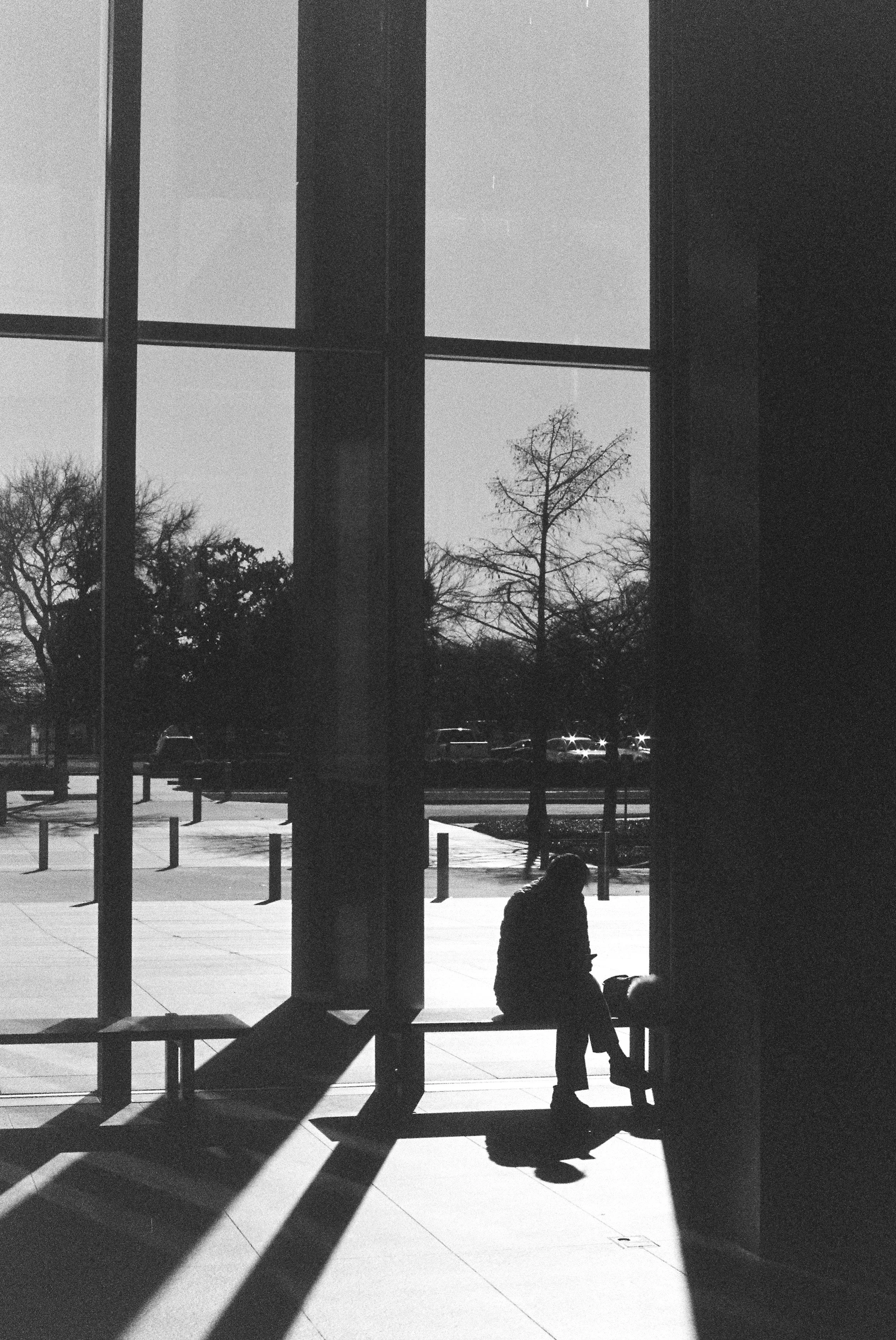 Silhouette of a person sitting on a bench inside the Modern Art Museum in Fort Worth, Texas, looking at their phone, in black and white 35mm film