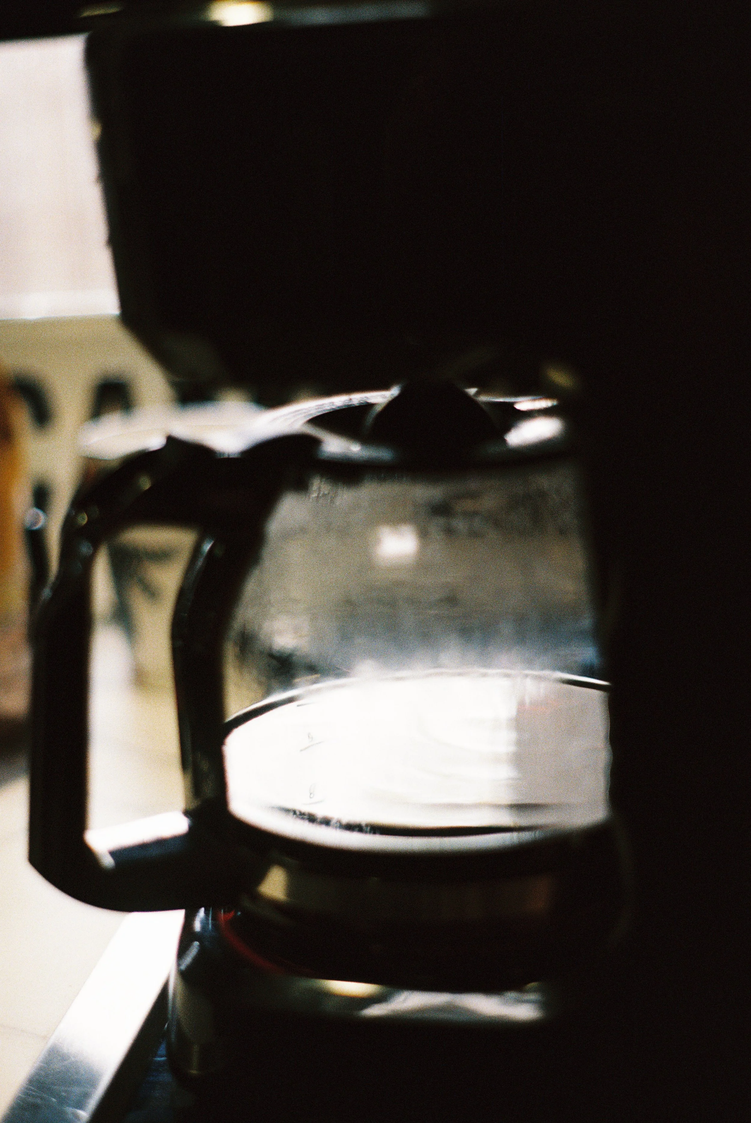 A glass coffee carafe under a coffee machine with a dark background.