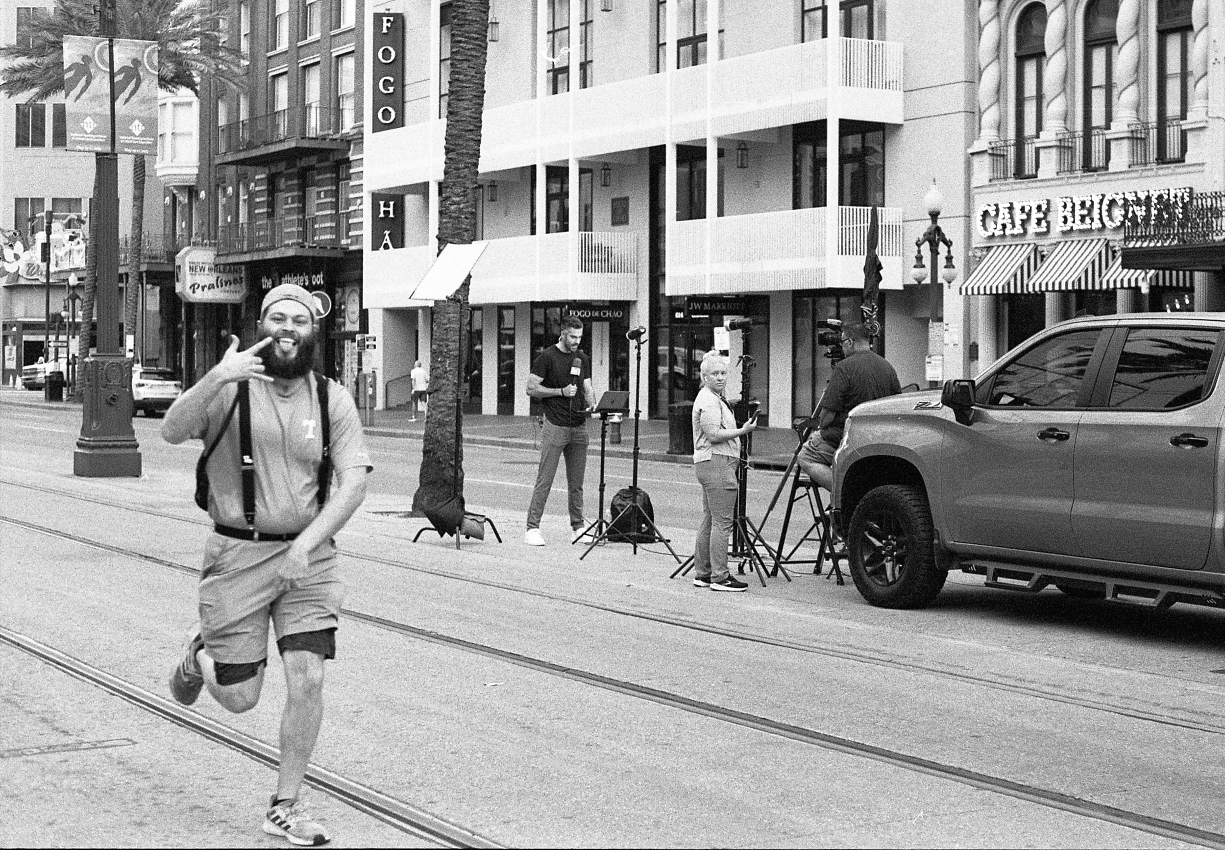 A runner is seen in the foreground "photobombing" while a news crew is in the background reporting live on Canal St in New Orleans