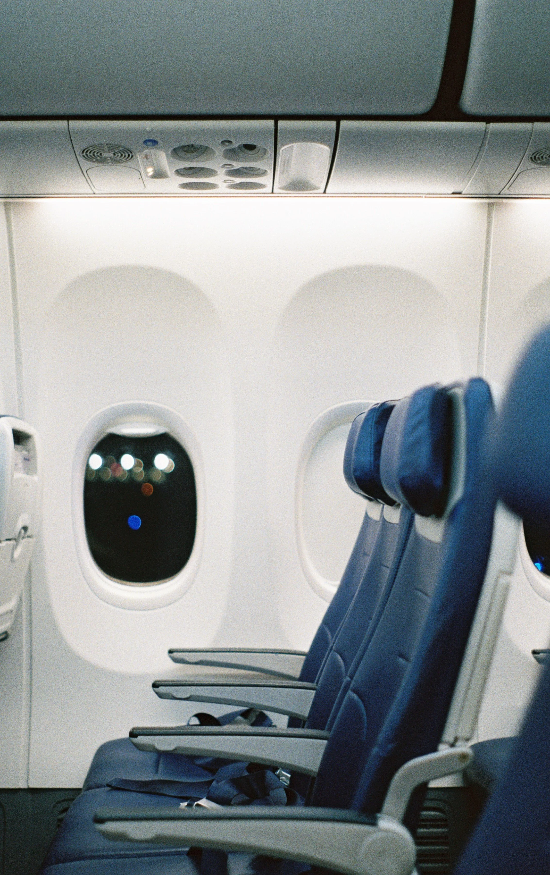 Inside an airplane cabin with empty blue seats and windows showing night scenery. Flying alone