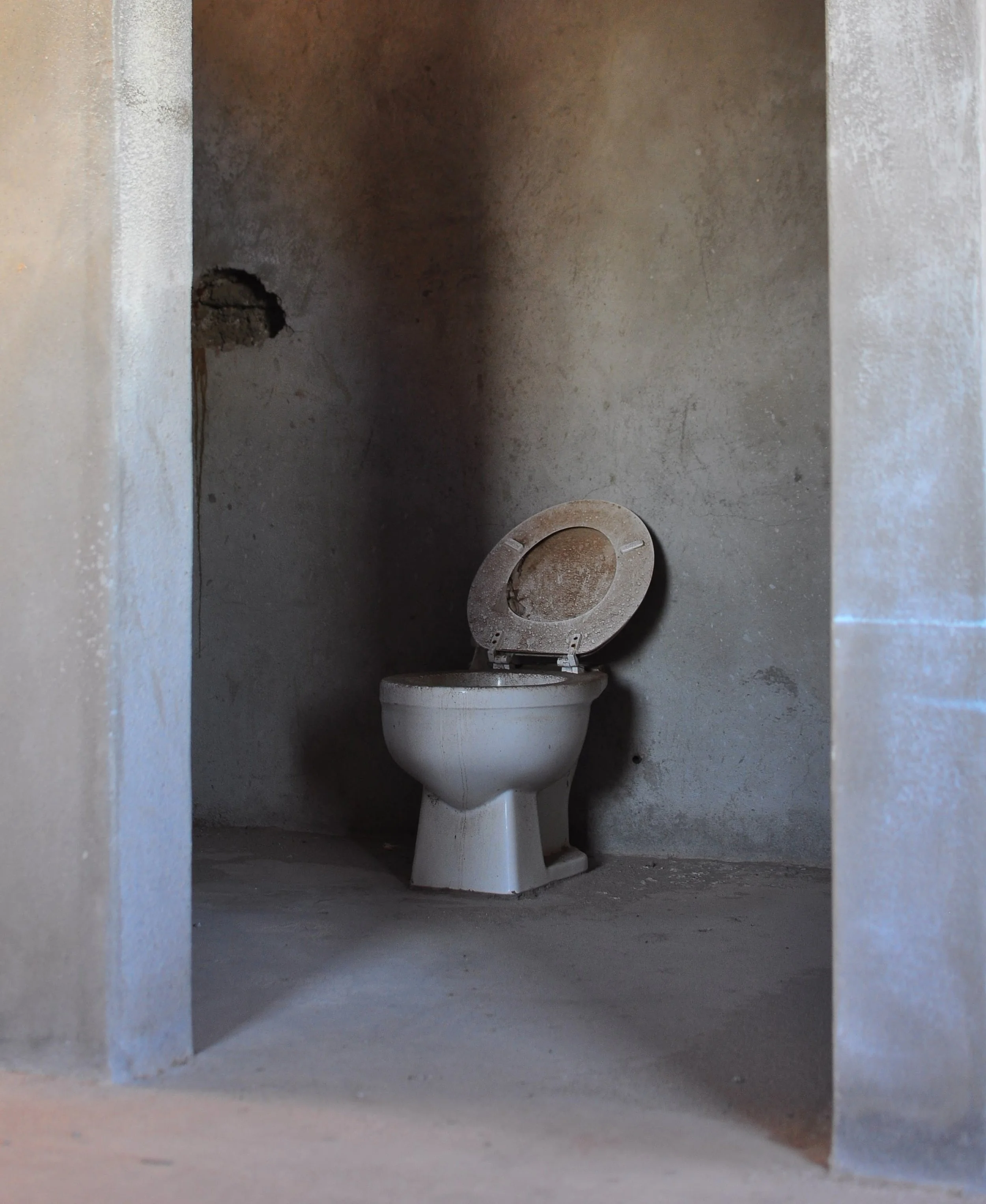 An abandoned and dirty toilet in a plain, unpainted concrete bathroom with a rough wall and floor. San Felipe, BCS Baja Mexico