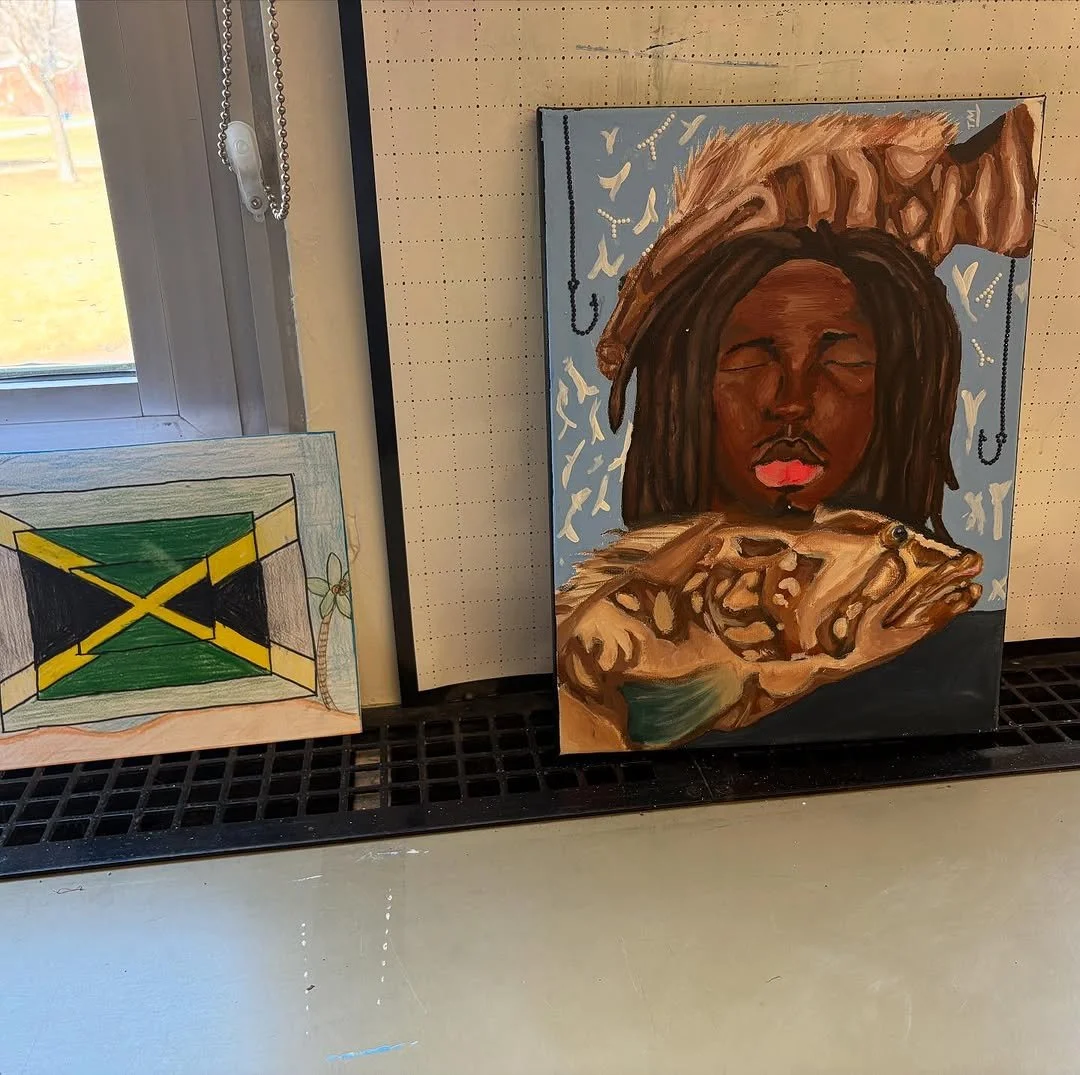 Colorful portrait painting of a woman with dark skin tone and dreadlocks, eyes closed, with a large hat on her head. To the left, a drawing of the Jamaican flag on paper.