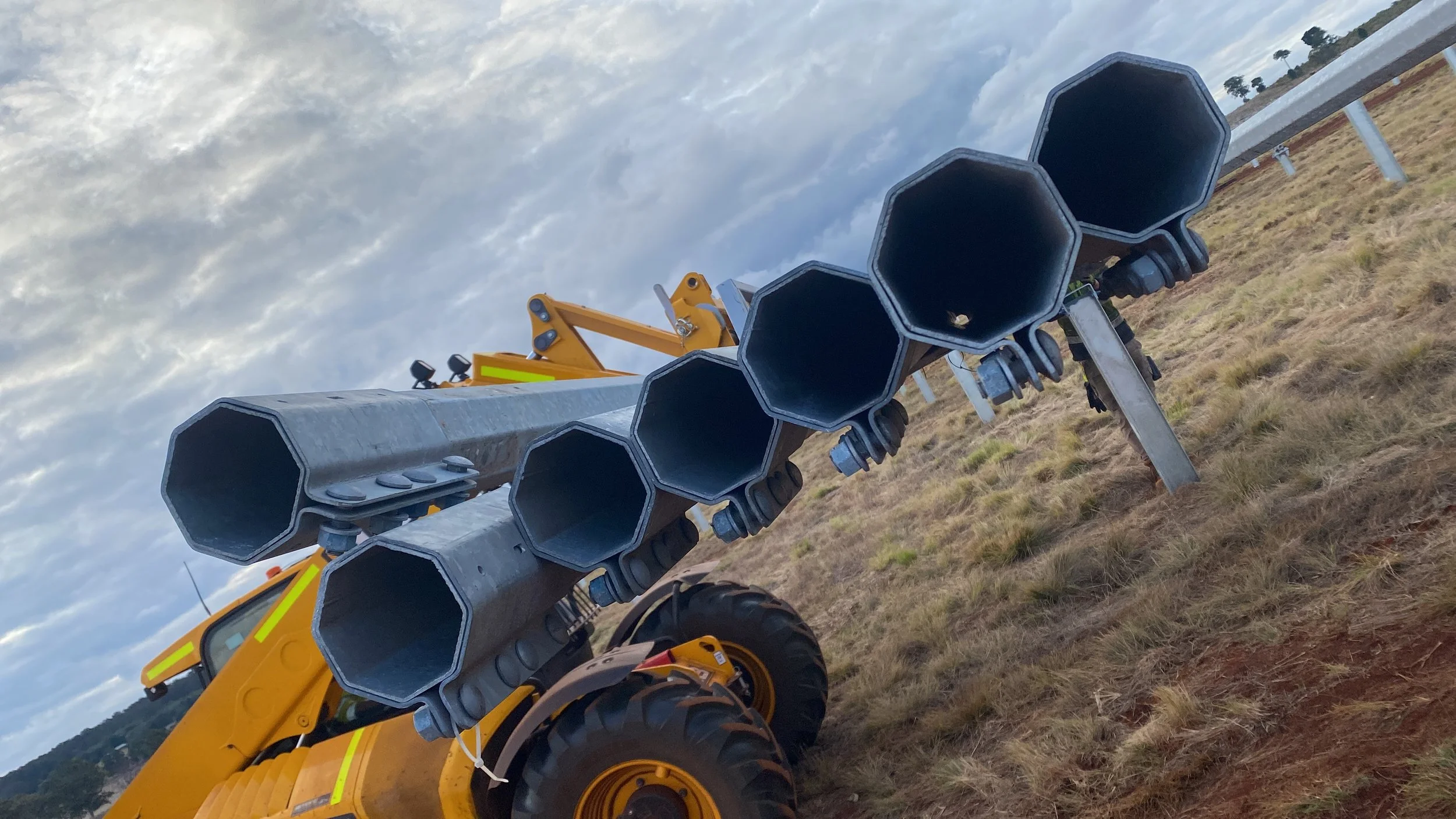 Close-up of a construction vehicle with large black pipes, possibly a fire truck, parked on a grassy field under a cloudy sky.
