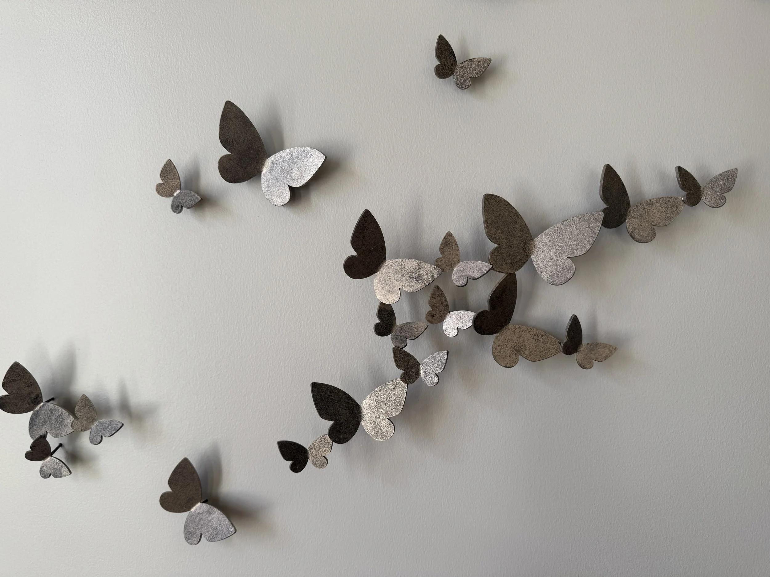 Decorative wall sculpture of butterflies in shades of black and silver on a light-colored wall.