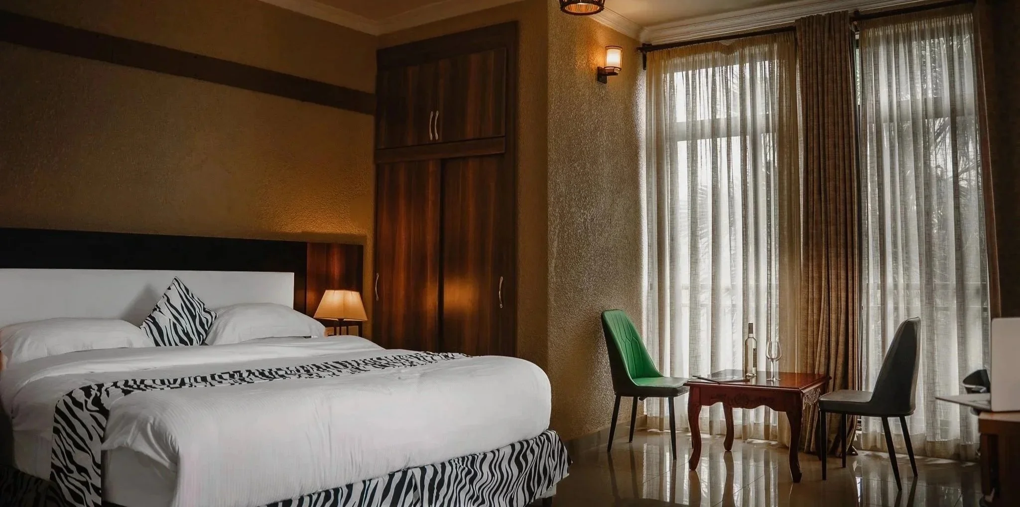 Quiet and comfortable hotel room with white bedding, zebra print accent, seating area, and large windows, offering a relaxing stay at Quality Inn Hotel Kigali, Rwanda.
