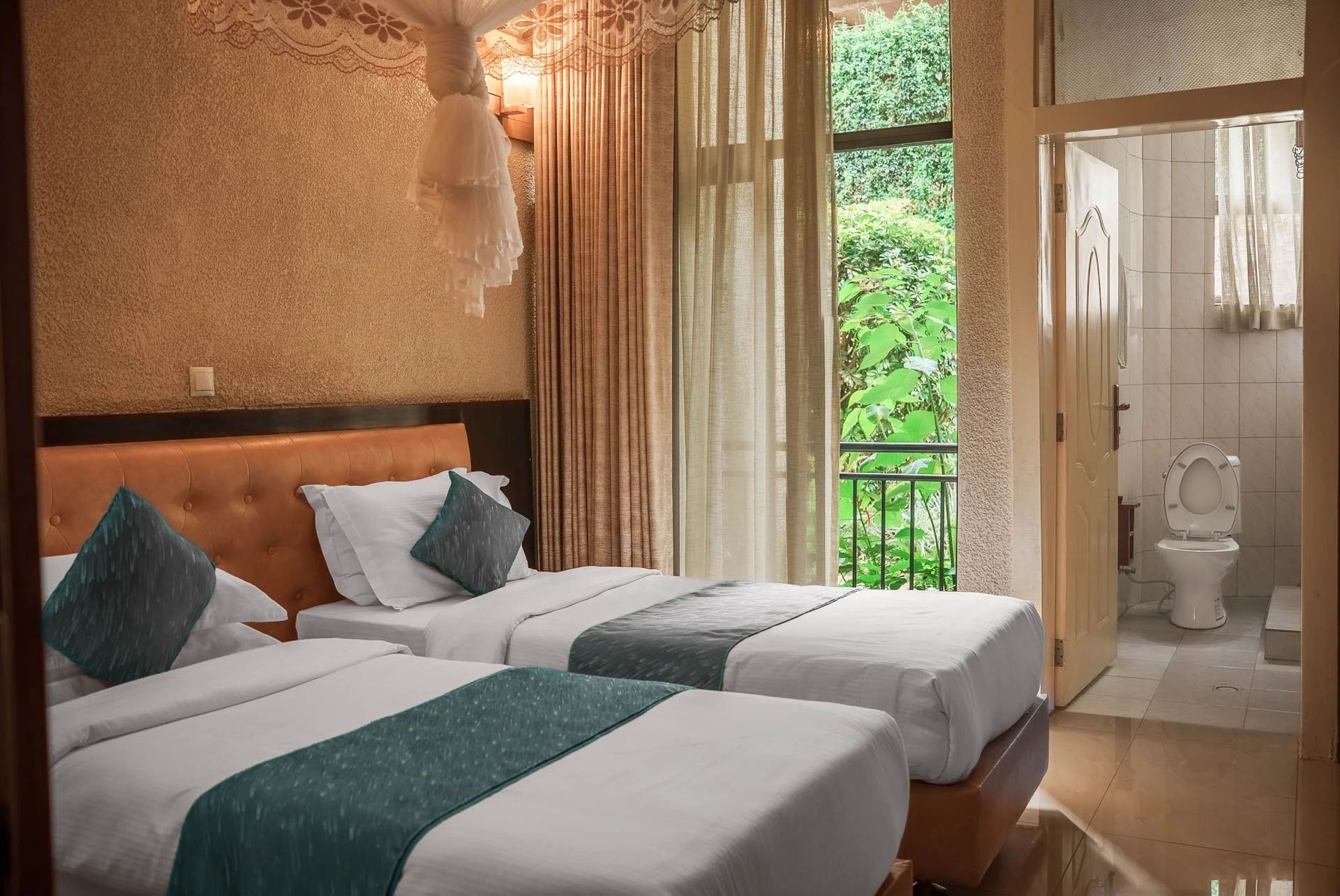 Deluxe Twin room at Quality Inn Hotel Kigali in Rwanda with two separate twin beds, warm lighting, a window with beige curtains overlooking lush greenery, and a private bathroom—quiet and suitable for friends or business travelers.